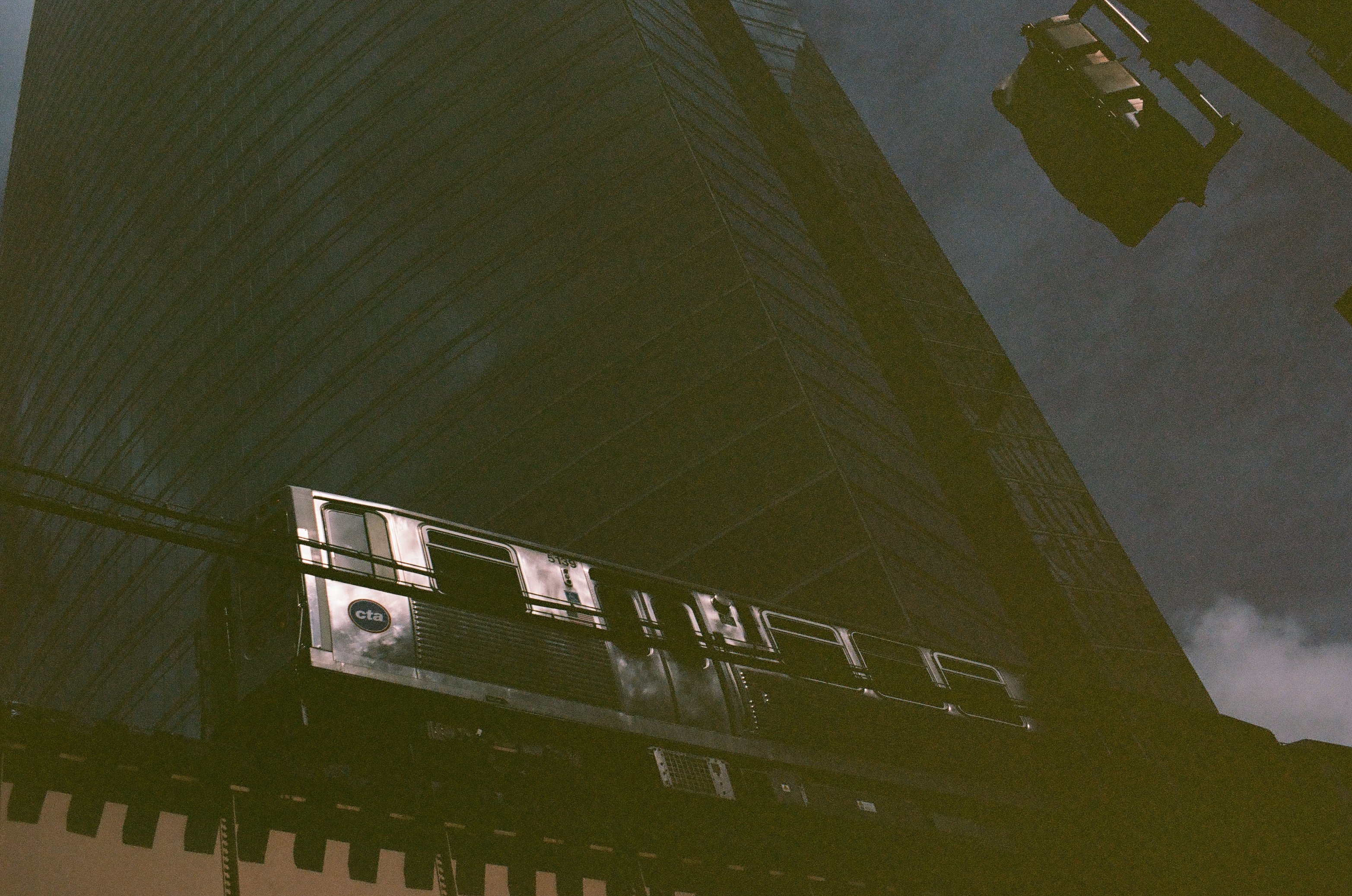 A rectangular sign hangs between steep dark facades as a narrow strip of clouded sky opens above.