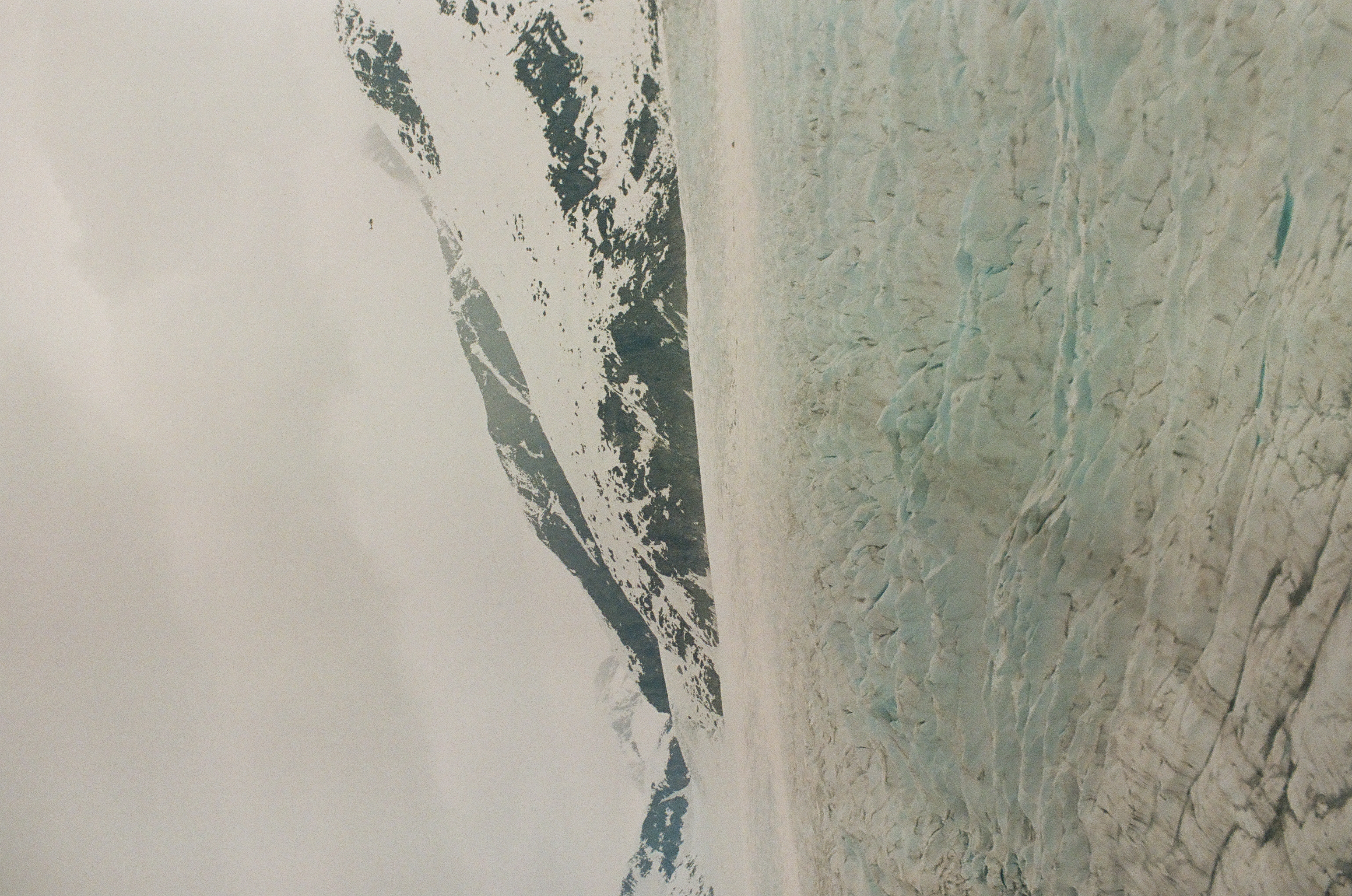 A pale blue wall of glacier ice rises beneath a smooth snowfield and partially hidden mountain slope.