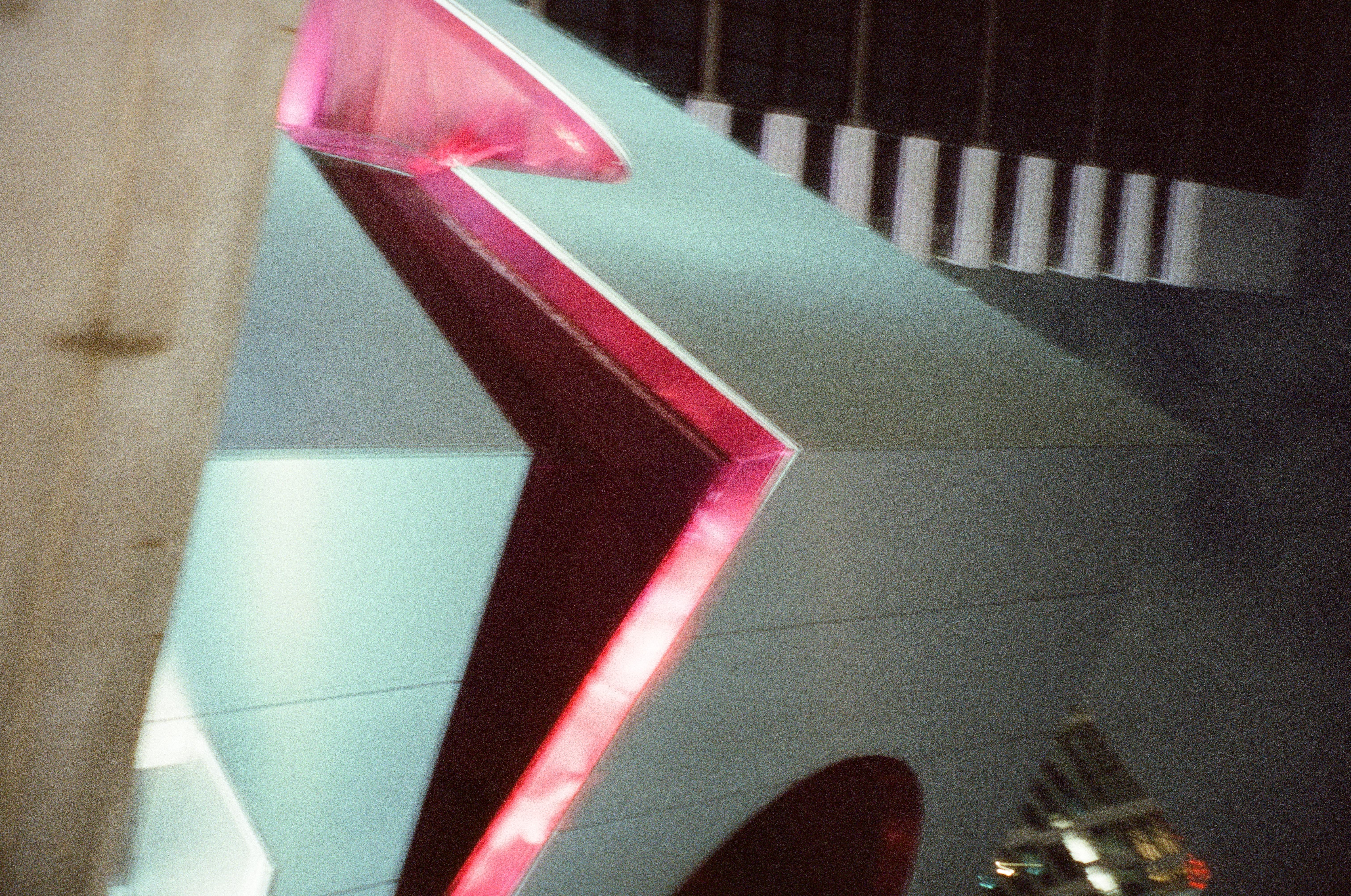 A bright pink line traces the corner of a building, with a striped tower visible at upper left and a red curved shape at right.