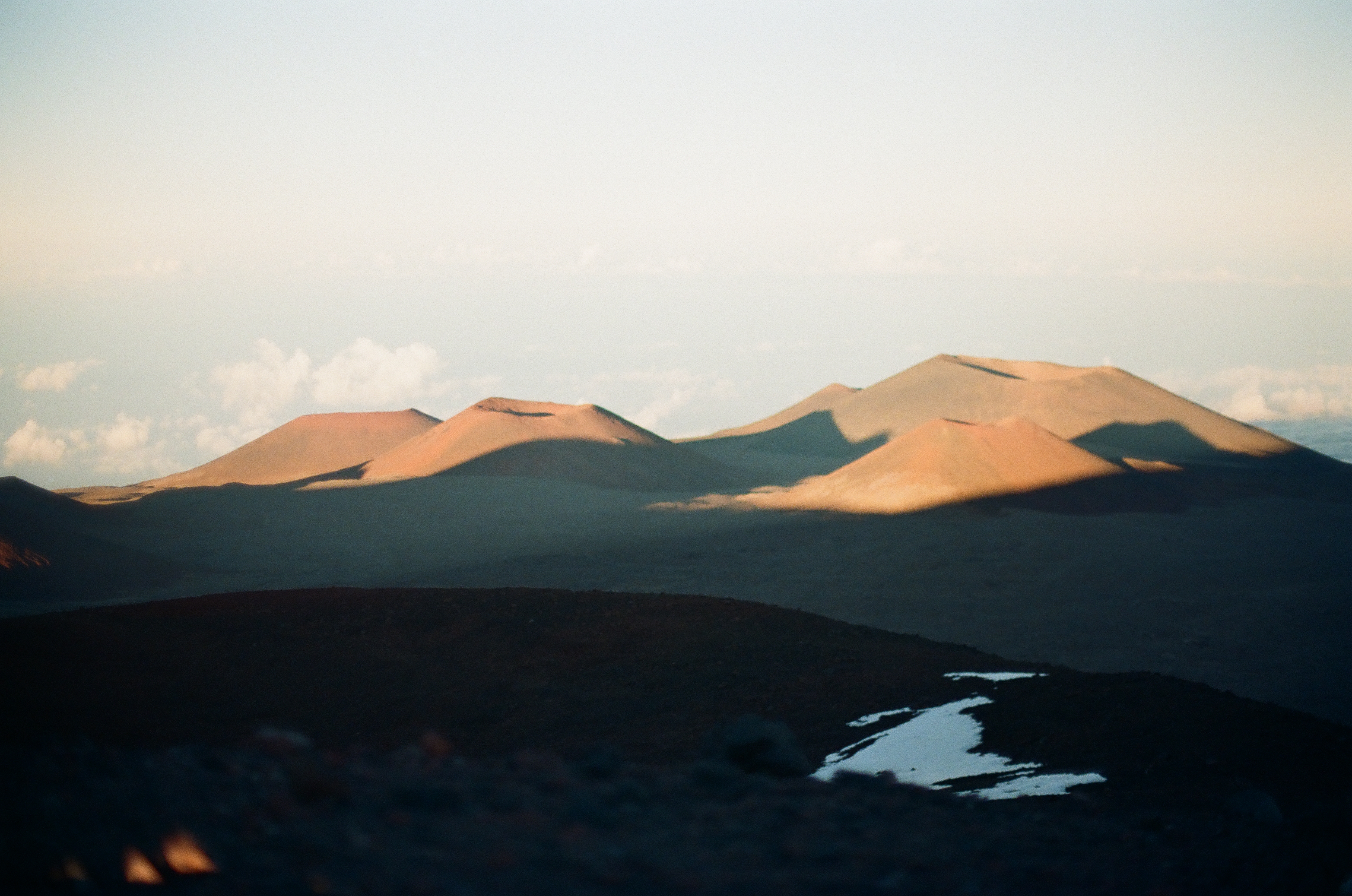 Warm light touches distant brown cones beyond a dark foreground streaked with melting snow.