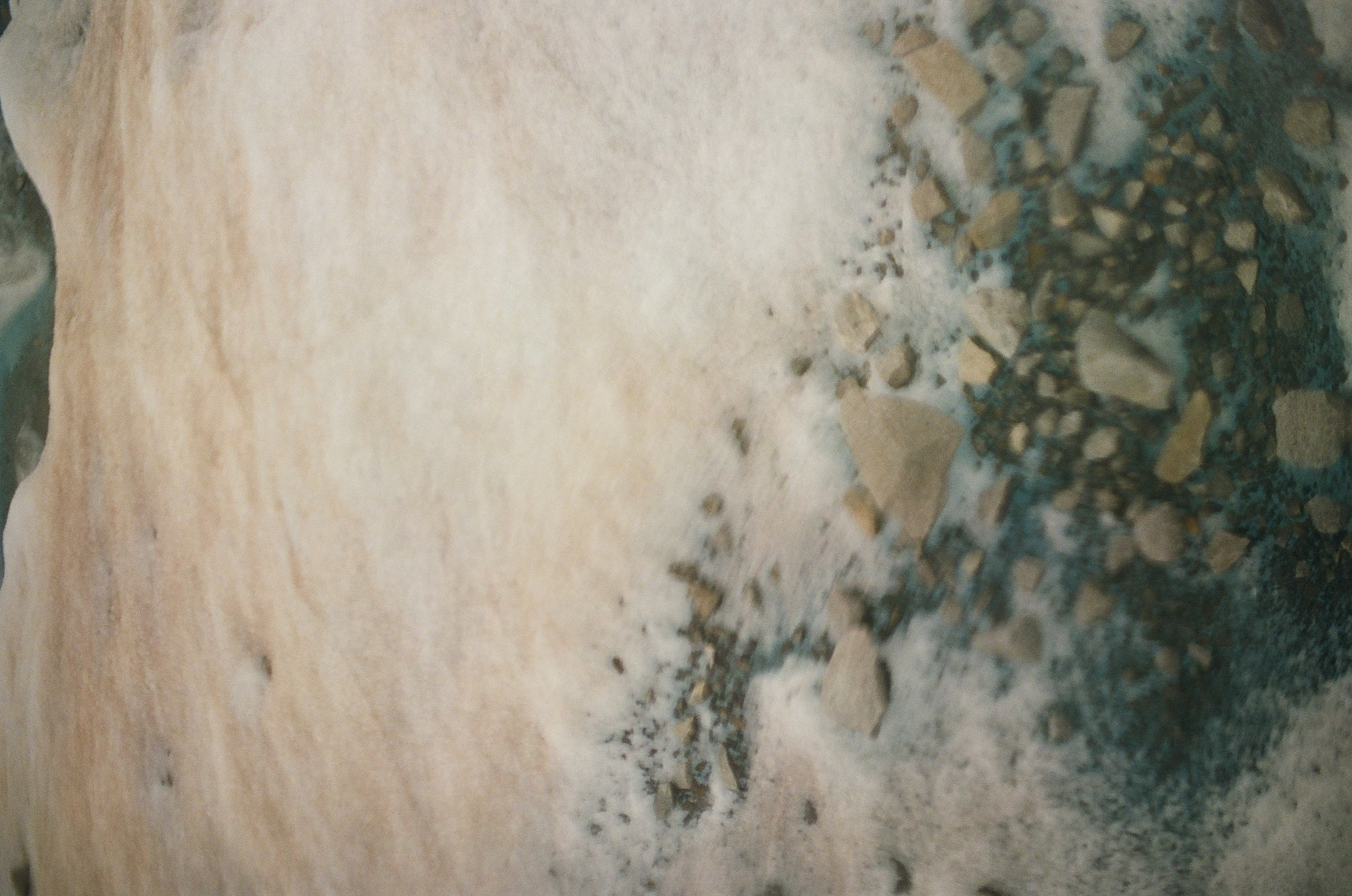Dark stones cluster beneath a thin uneven snow cover in a close view of mottled ground.