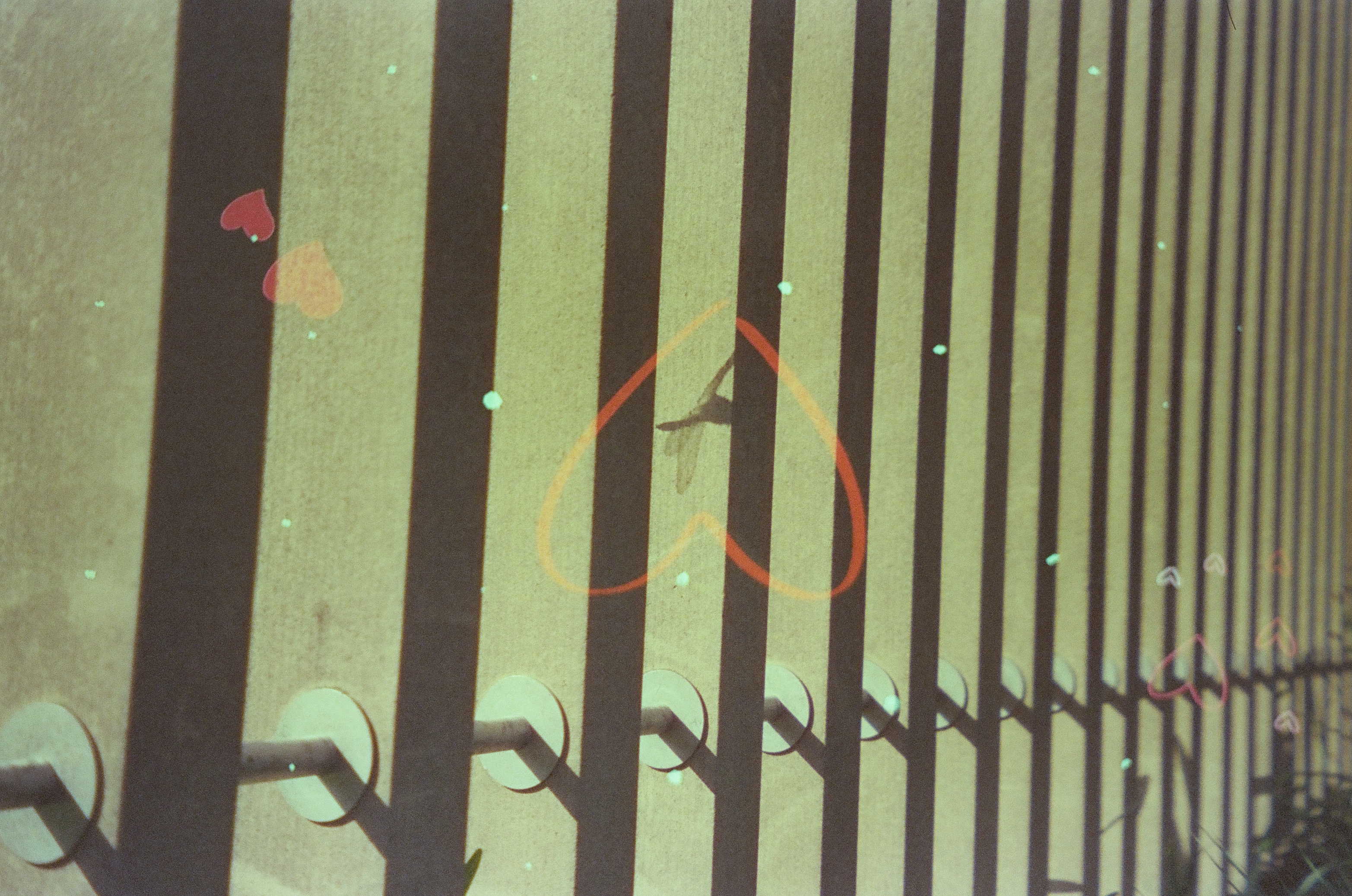 Diagonal shadow stripes from a railing fall across a pale wall, overlaid with two small heart shapes, one larger heart outline, and small heart outlines near the right edge.