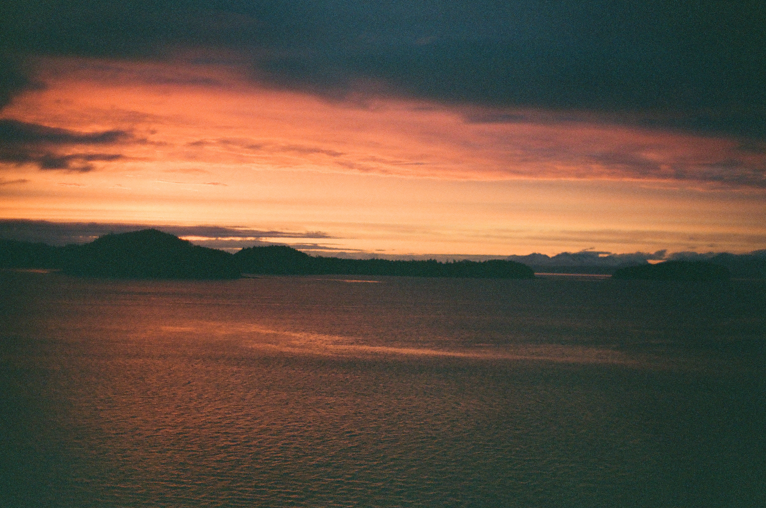 A broad orange horizon stretches behind dark islands while copper light crosses textured open water.