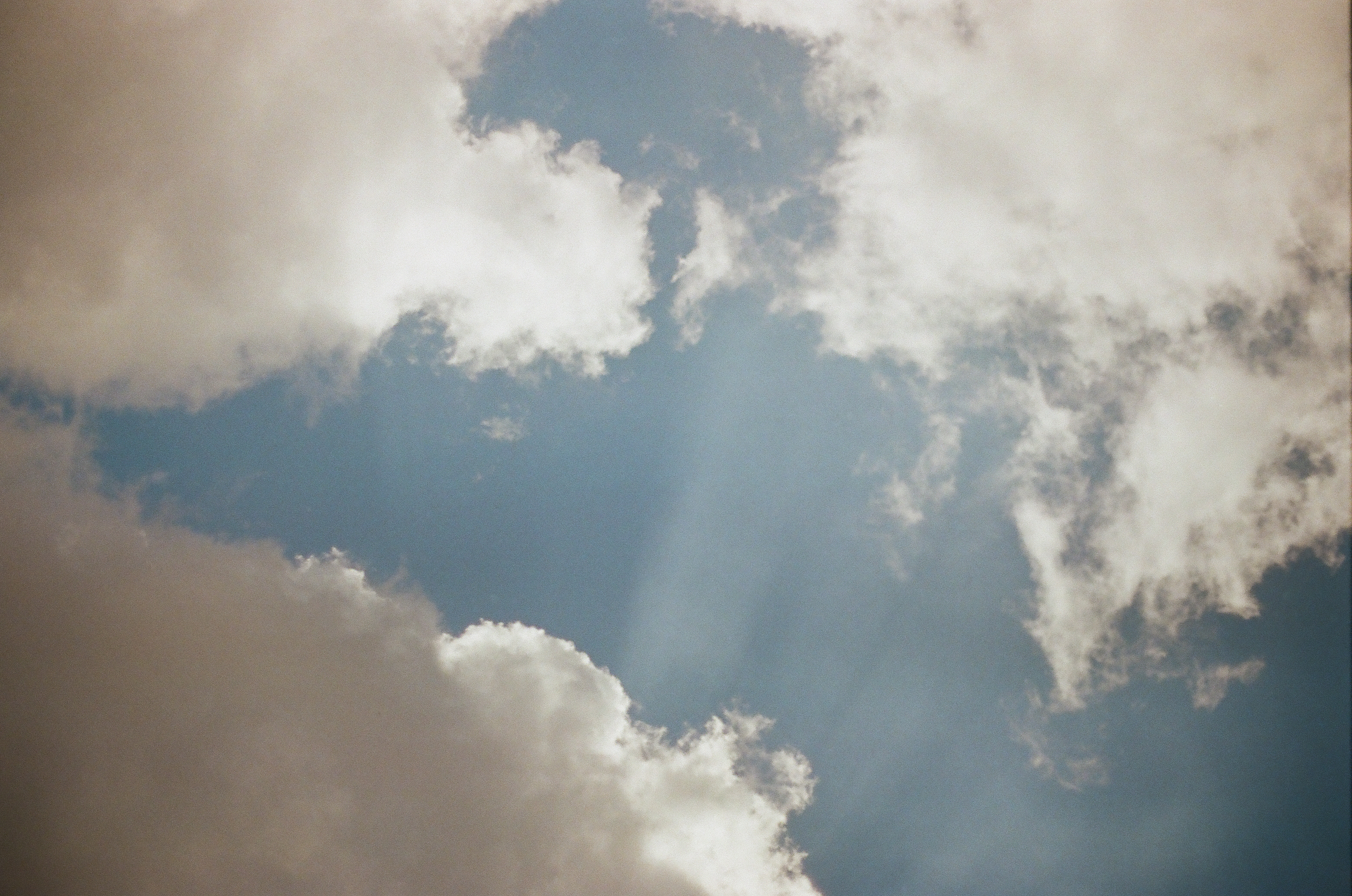 Sunbeams pass through a broken ring of bright white cloud into a clear blue opening.