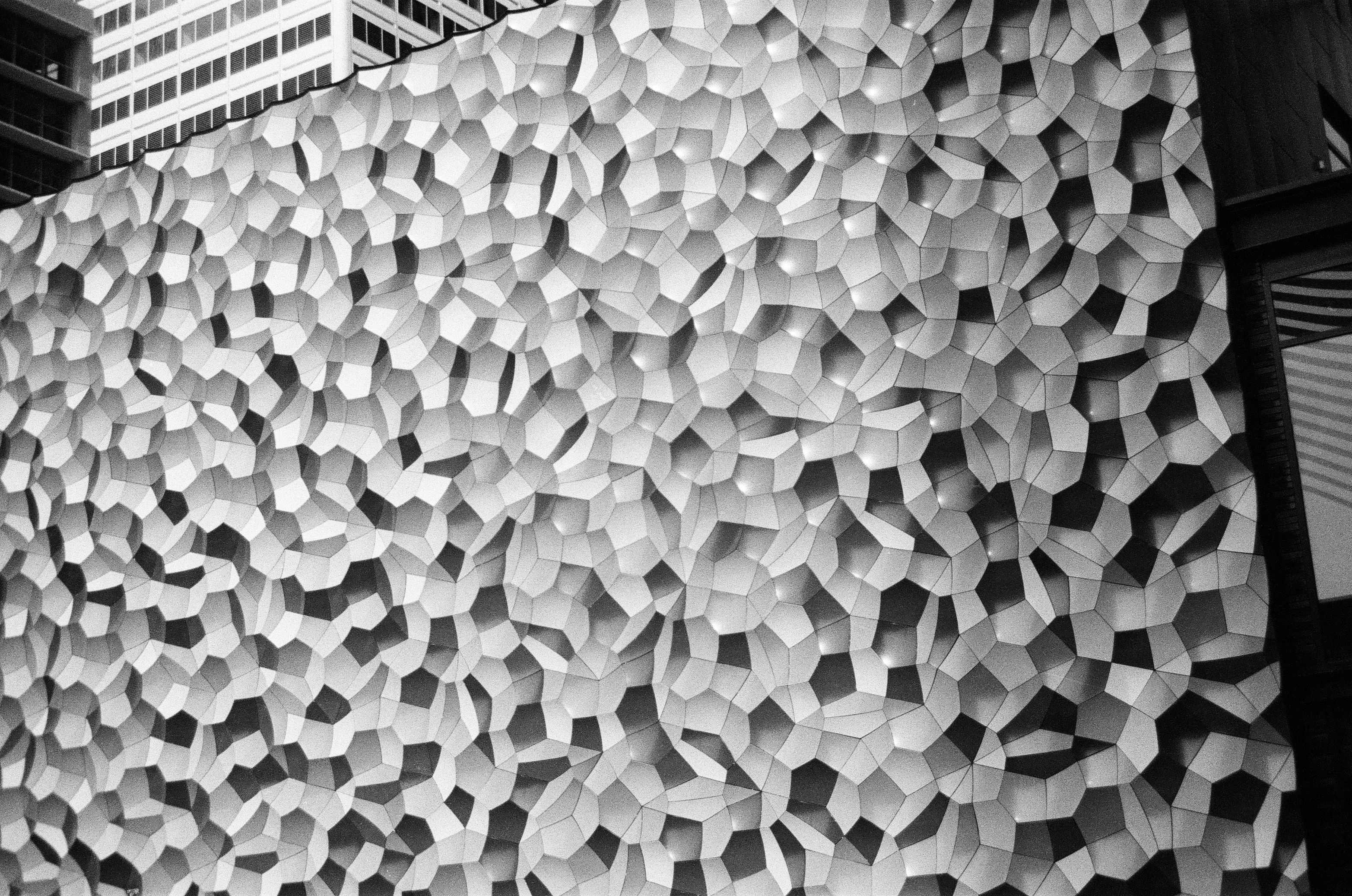 Hundreds of irregular raised wall facets catch alternating bands of pale light and deep shadow.