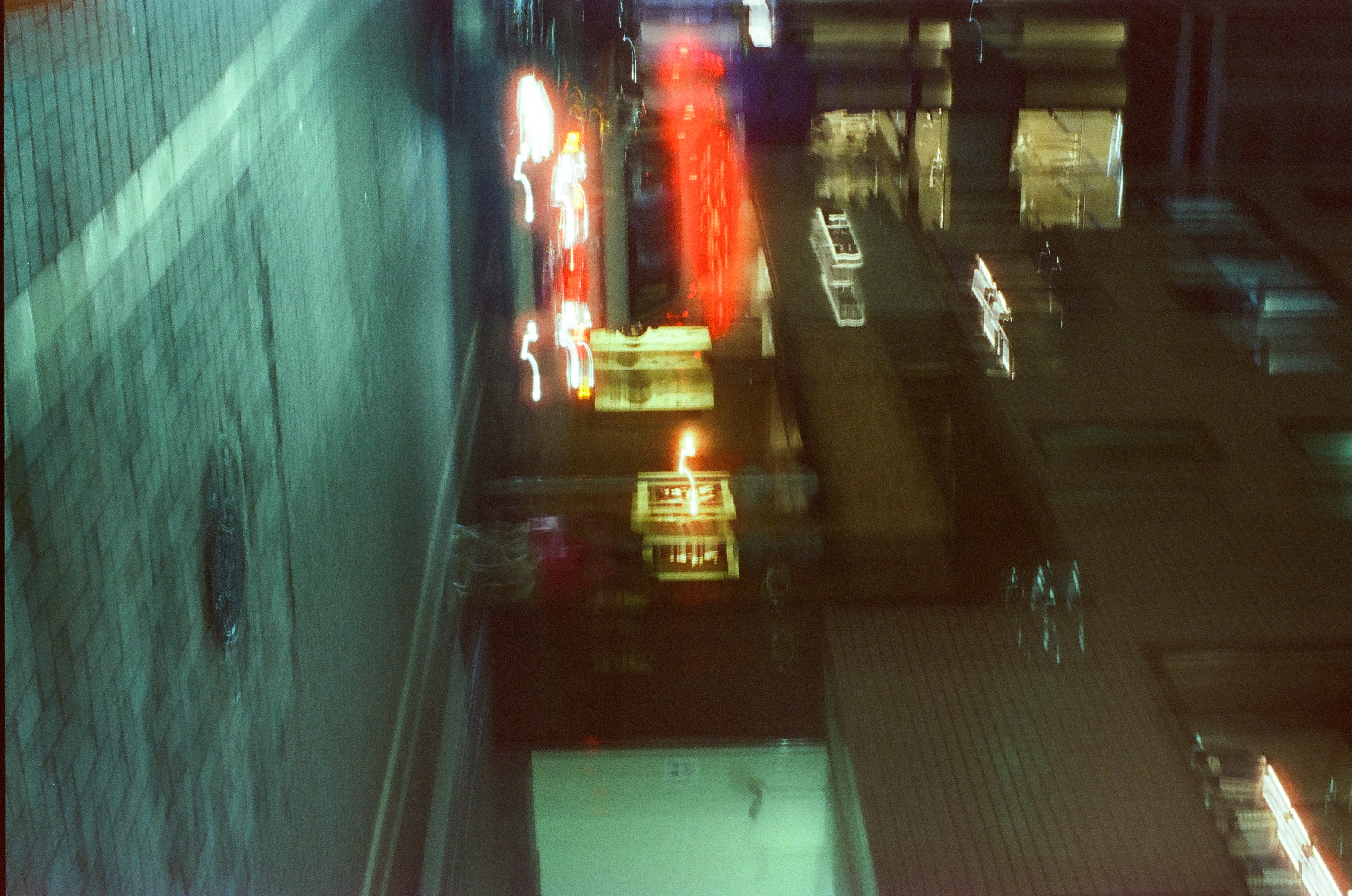 Motion blur turns a night street into diagonal streaks of red and gold light above a tiled wall and glossy wet pavement.
