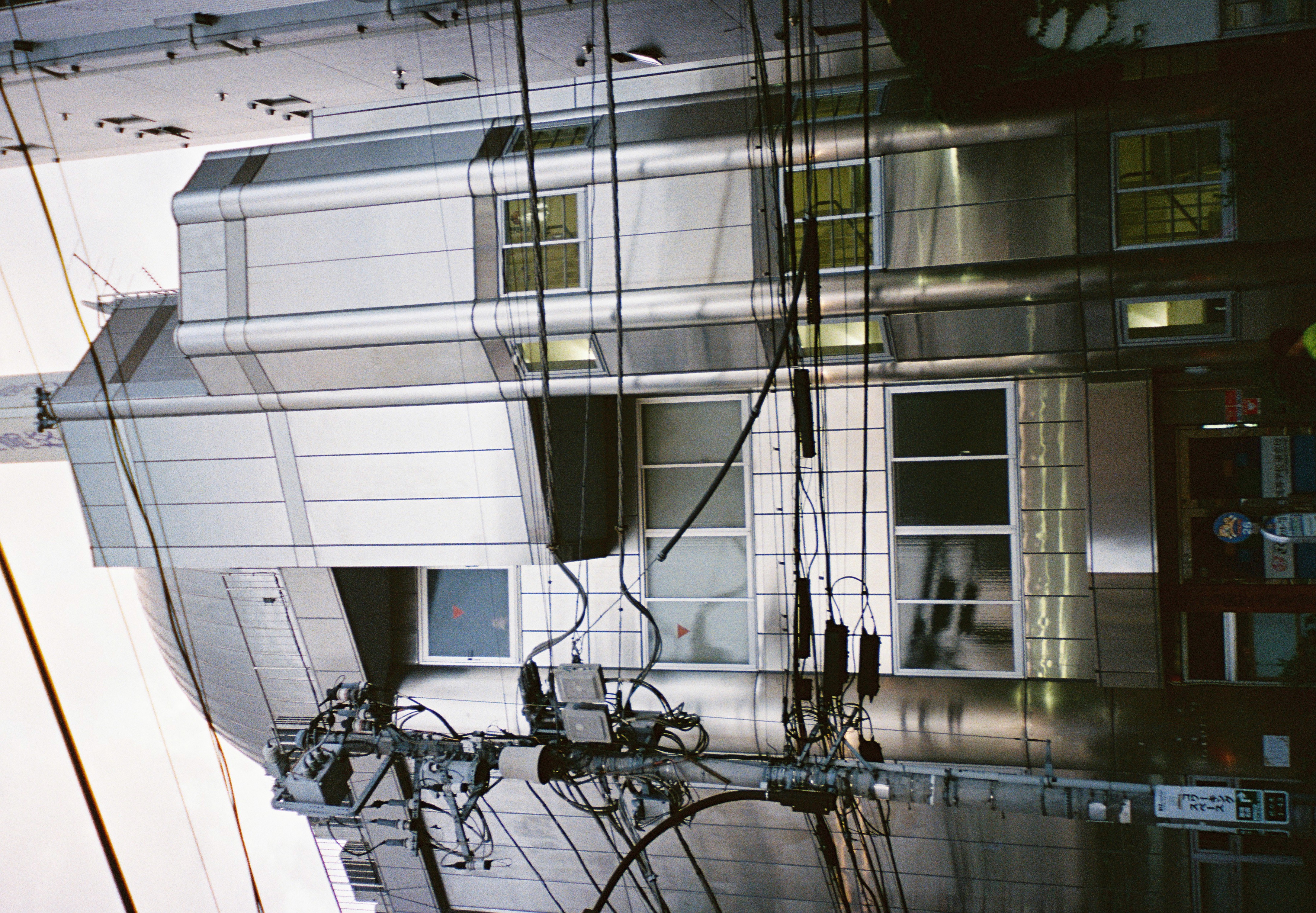 Dense utility wires cross a narrow white building with balconies, pipes, and rooftop equipment.