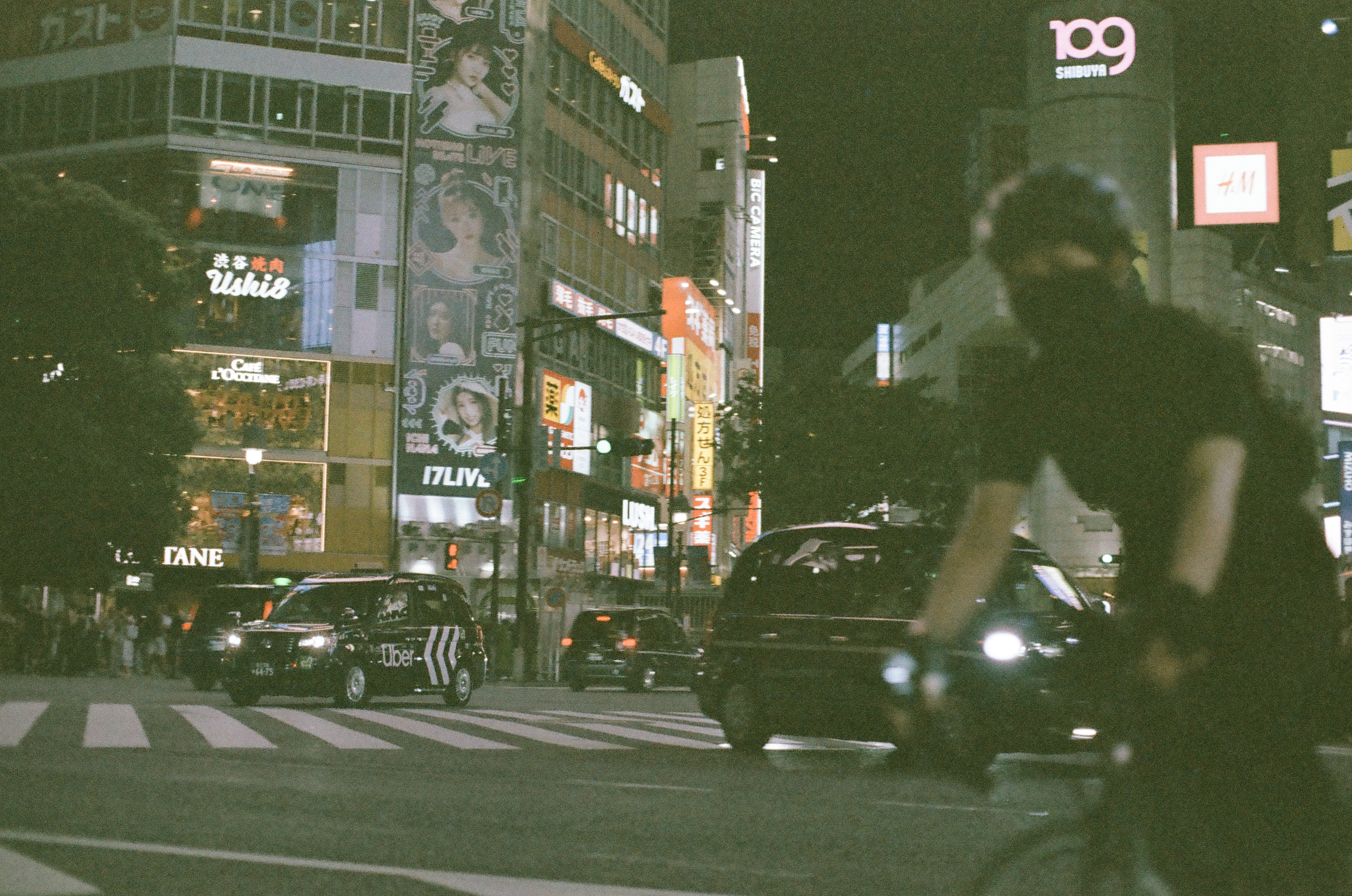 A motion-blurred cyclist wearing a mask and helmet crosses in front of a taxi and other cars stopped at a crosswalk.