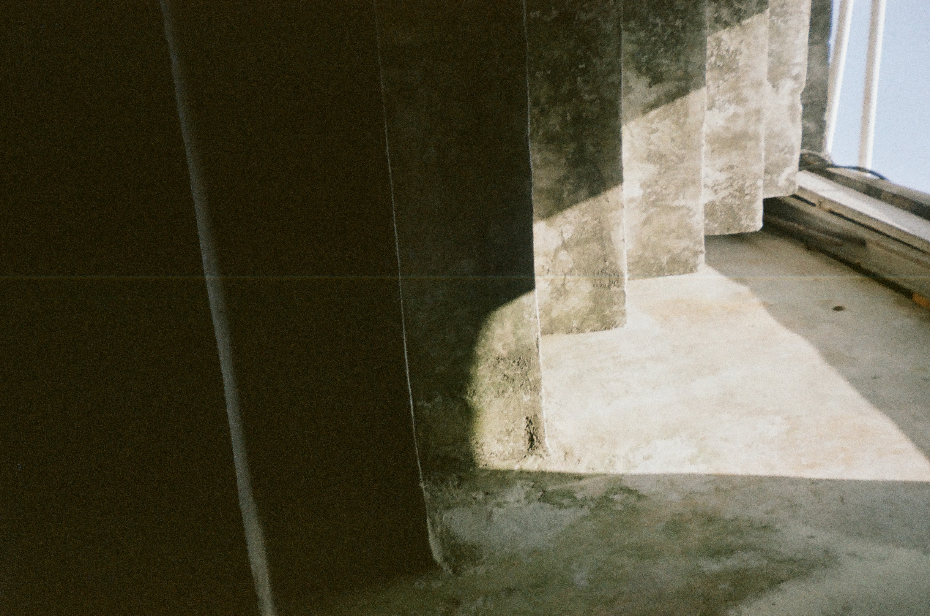 Rough concrete stairs rise beside a tall wall, with angular sunlight and shadow dividing the weathered surfaces.