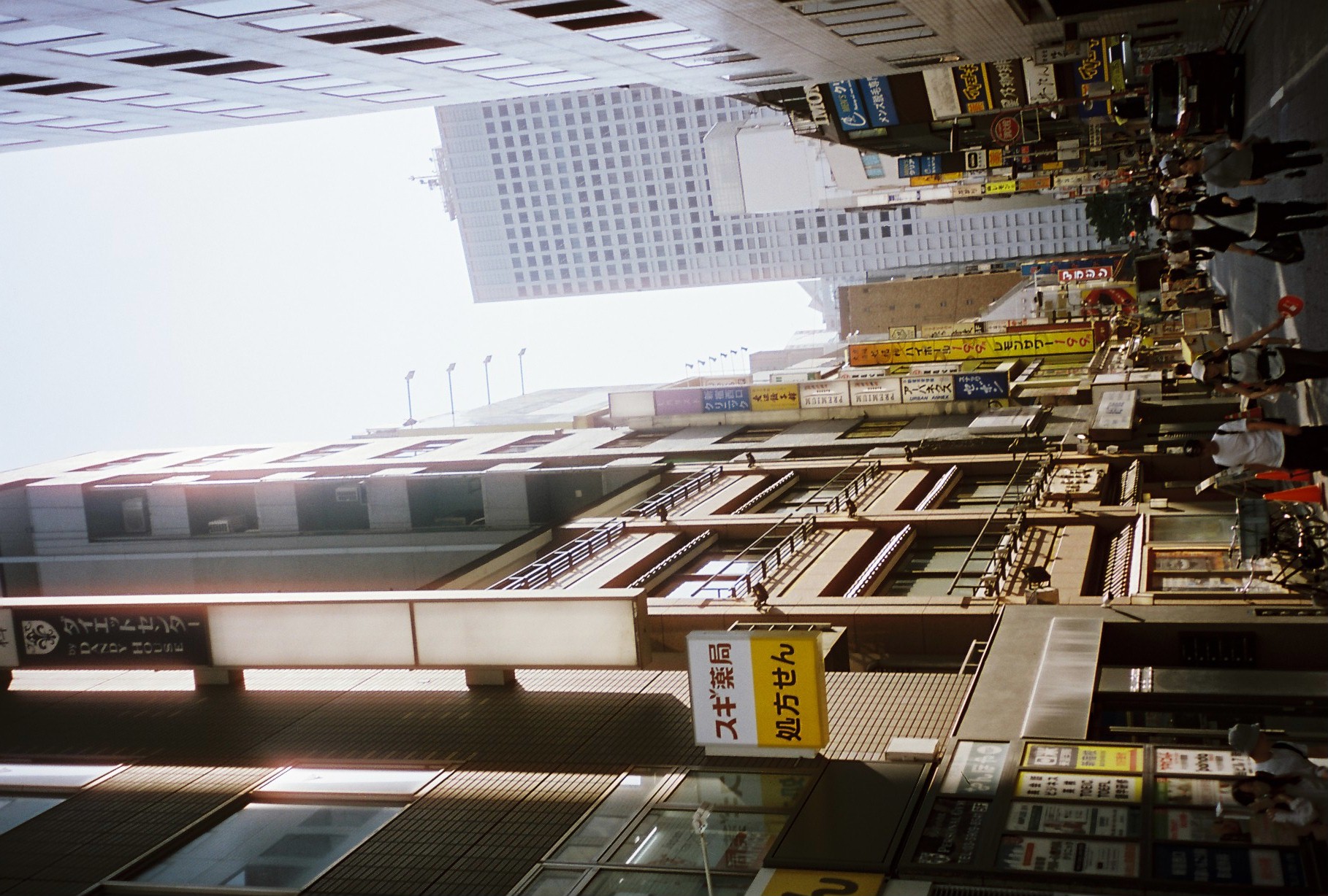 Vertical signs, including a yellow pharmacy placard and a black Dandy House banner, stack a narrow street leading toward a hazy high-rise.
