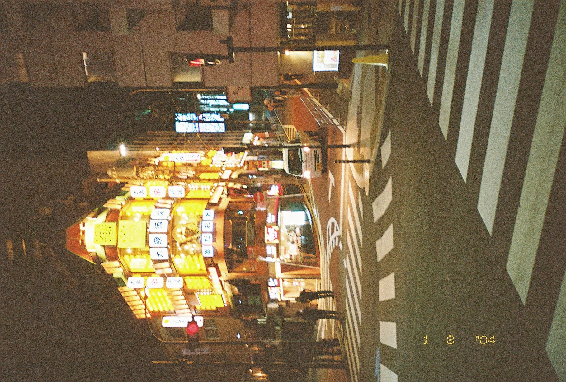A wedge-shaped corner building is covered floor to floor in illuminated amber signage, including a panel reading 大衆酒場, above an empty crosswalk intersection.