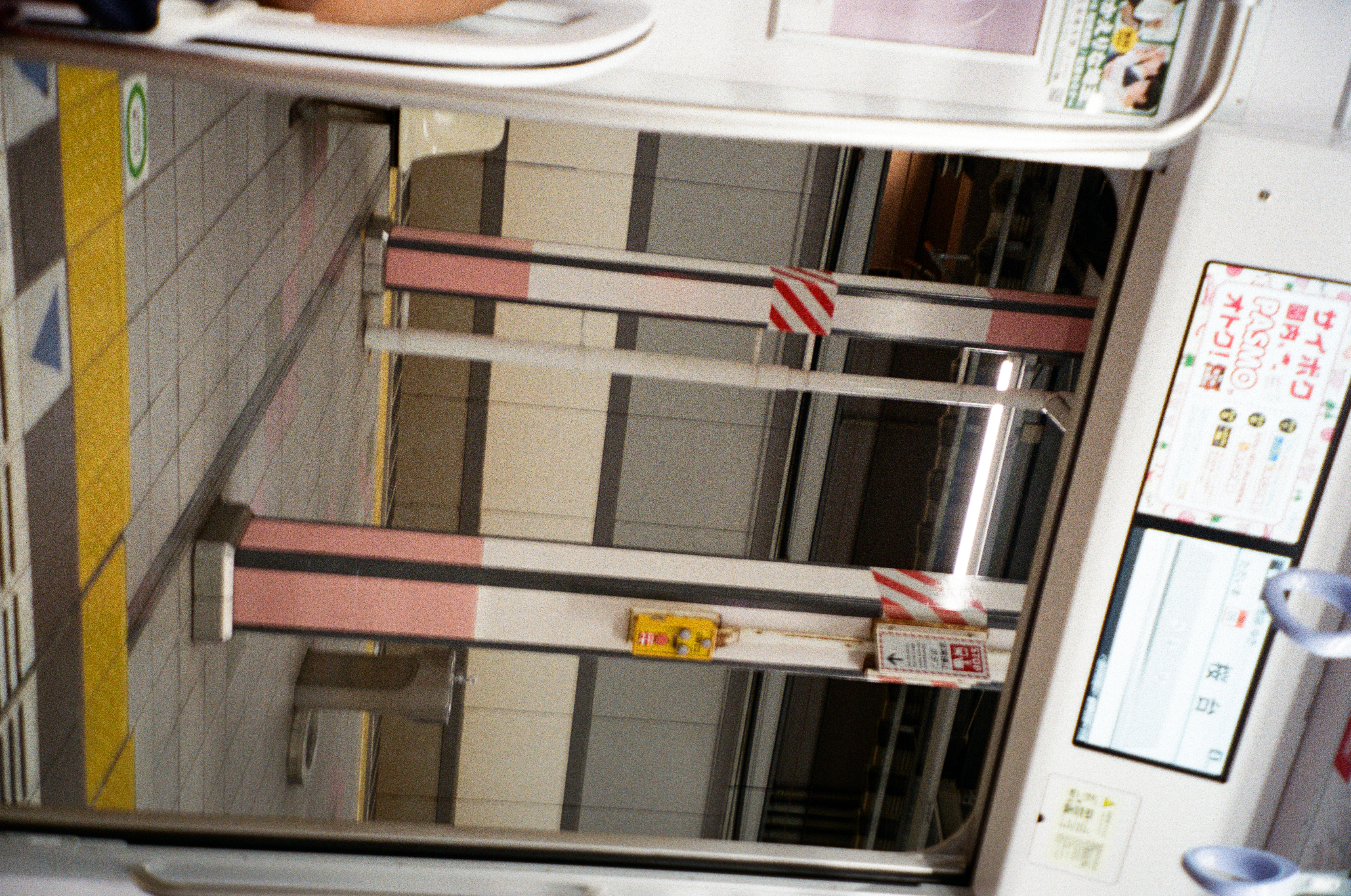 Open train doors frame a platform with pink-and-gray striped pillars, red hazard tape, and a stainless drinking fountain under fluorescent light.