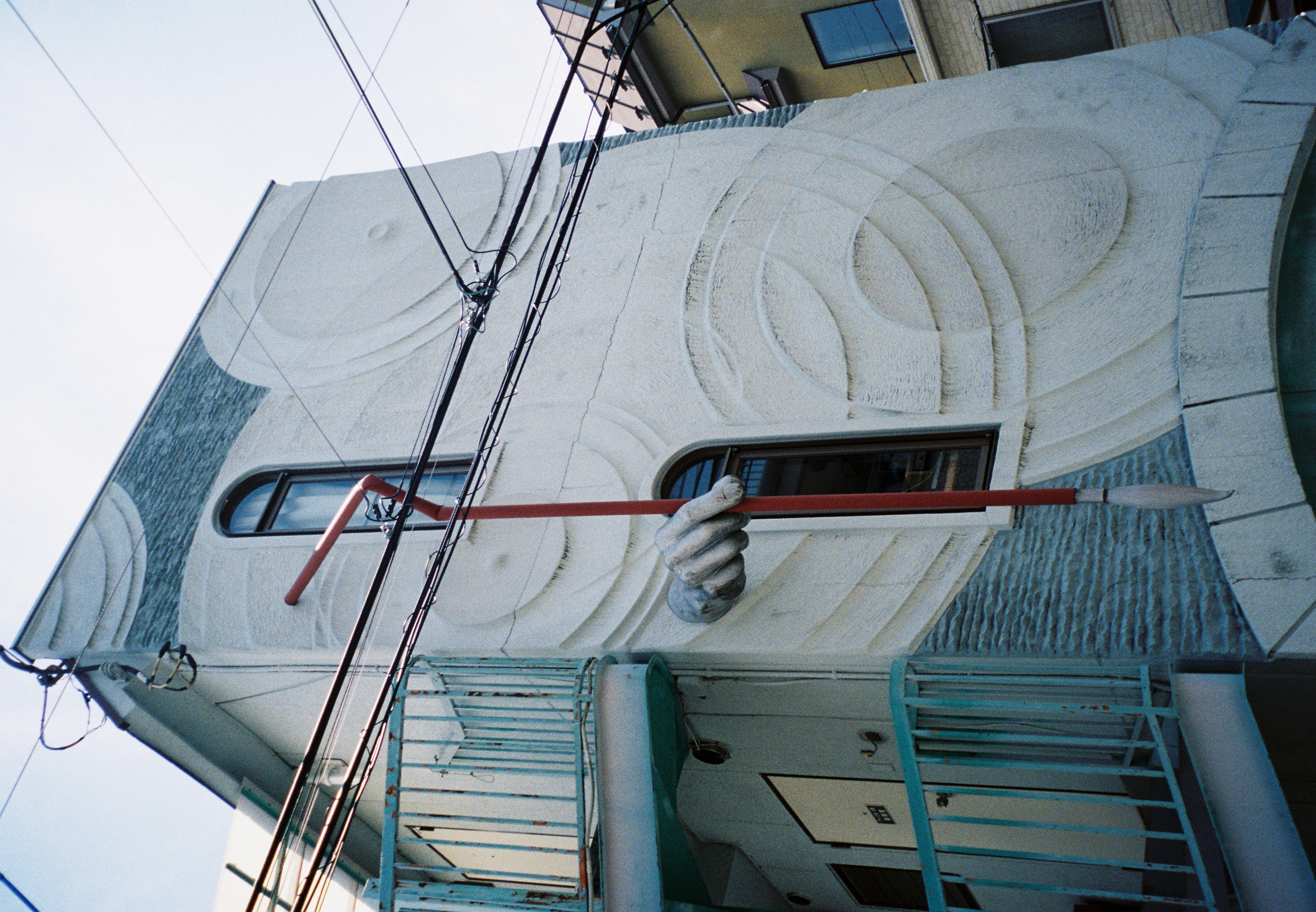 A carved relief hand grips a long red pole against a textured white building facade with arched windows and circular carved patterns.