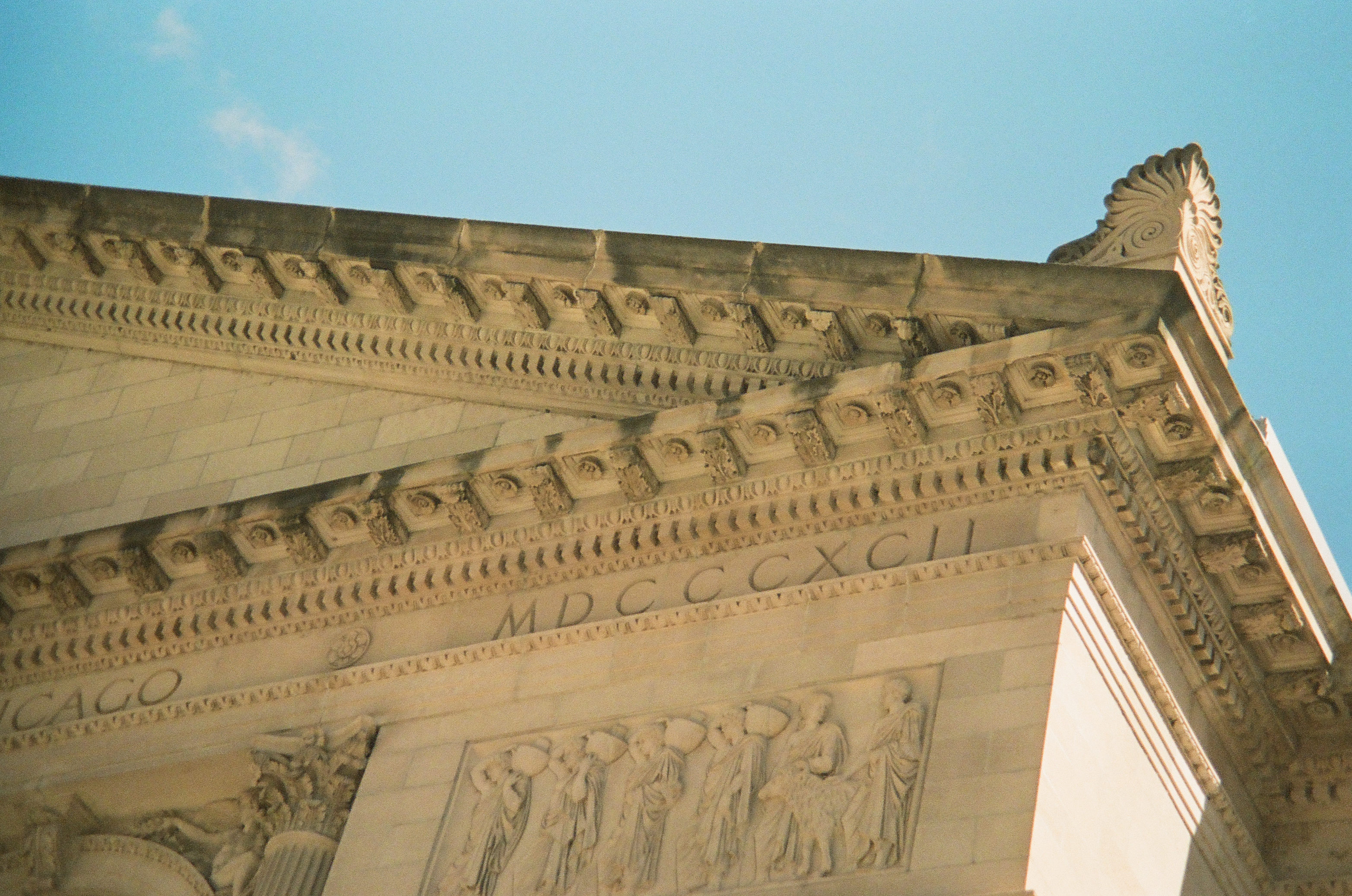 Carved figures and Roman numerals stretch beneath an ornate stone cornice against blue sky.