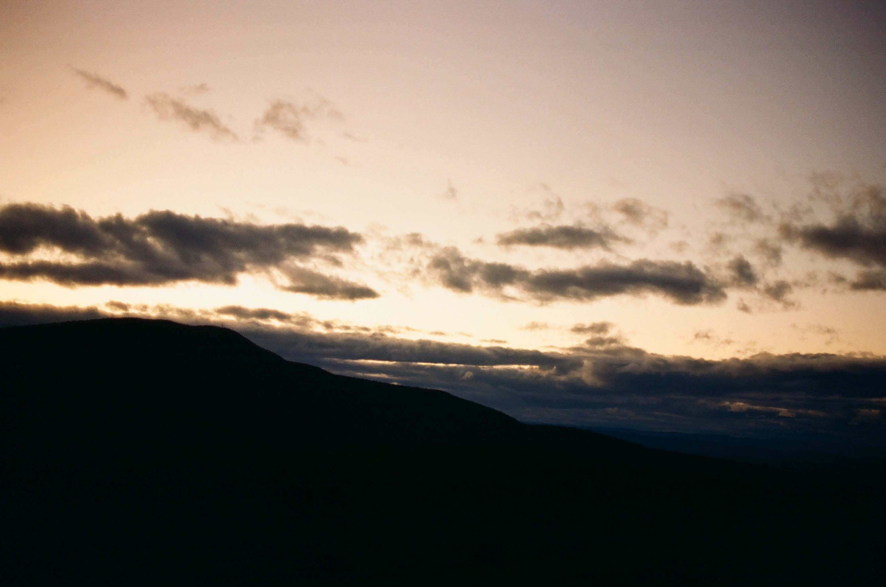 A mountain ridge reads as a solid black silhouette beneath a sky banded with peach, gray, and lavender cloud.