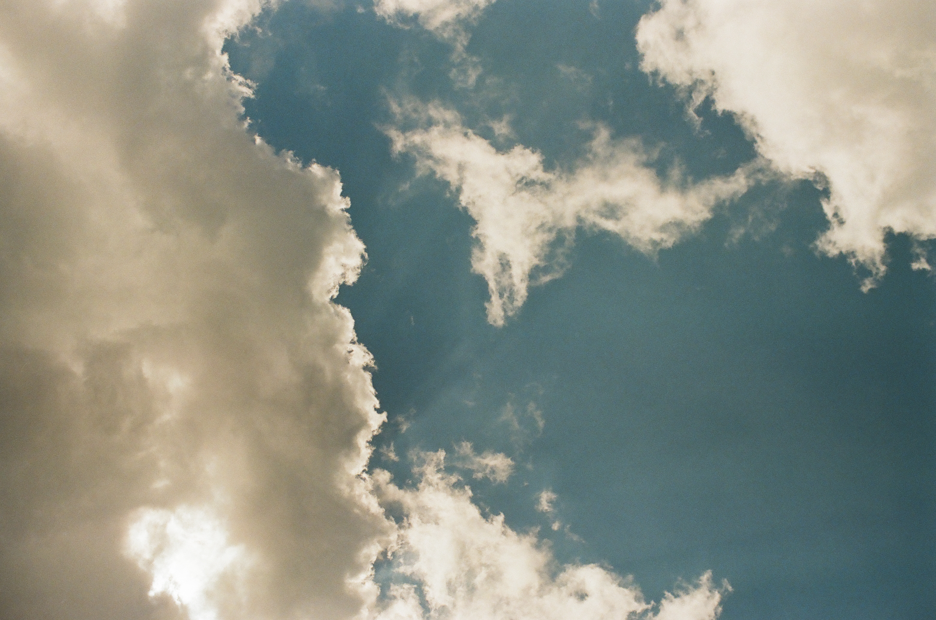 Bright white clouds part around a deep blue opening while sunlight glows through one silver edge.
