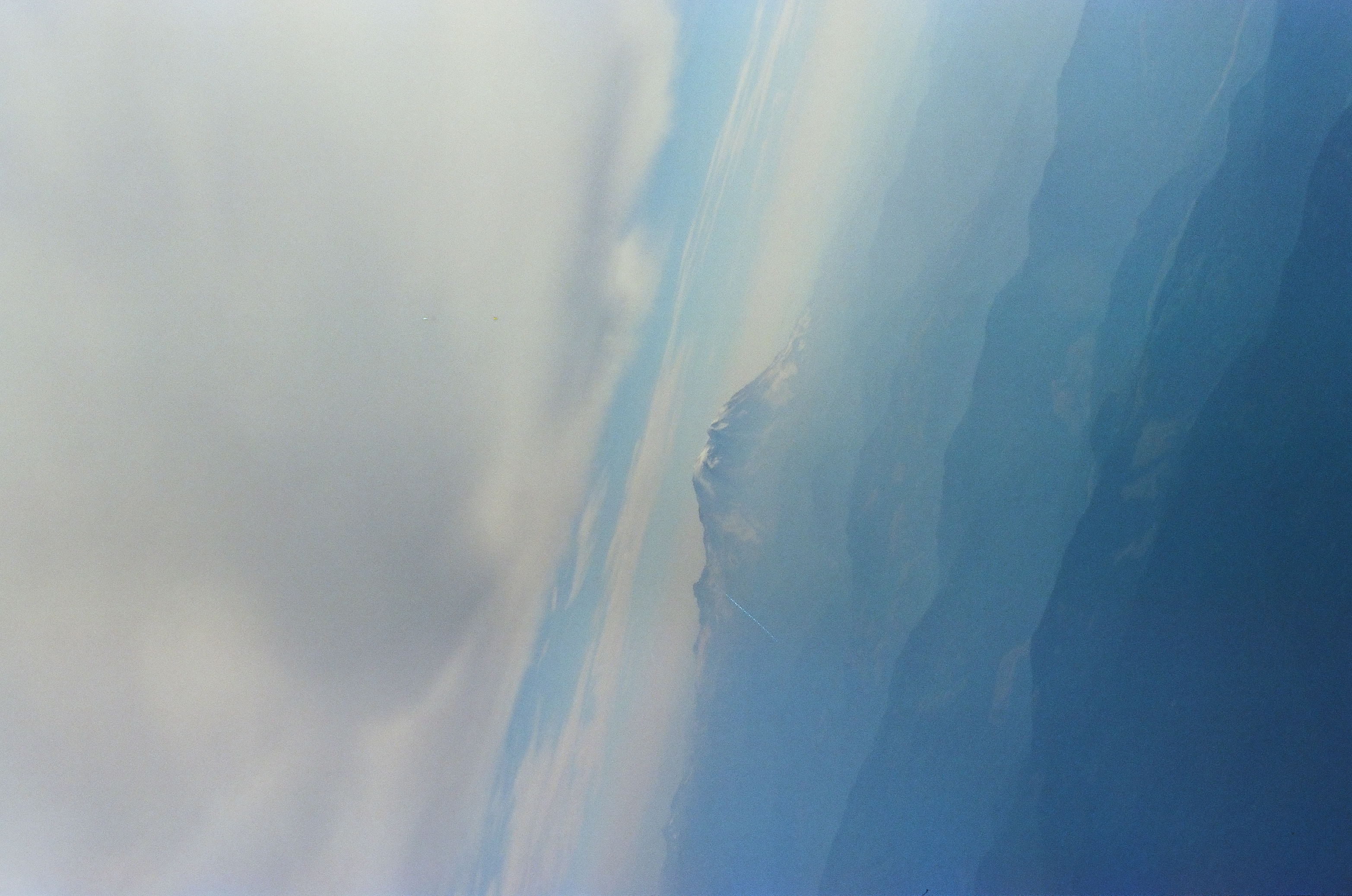 A vertical composition shows a small snow-capped peak below a heavy shelf of cloud, with layered ridgelines extending beneath it.
