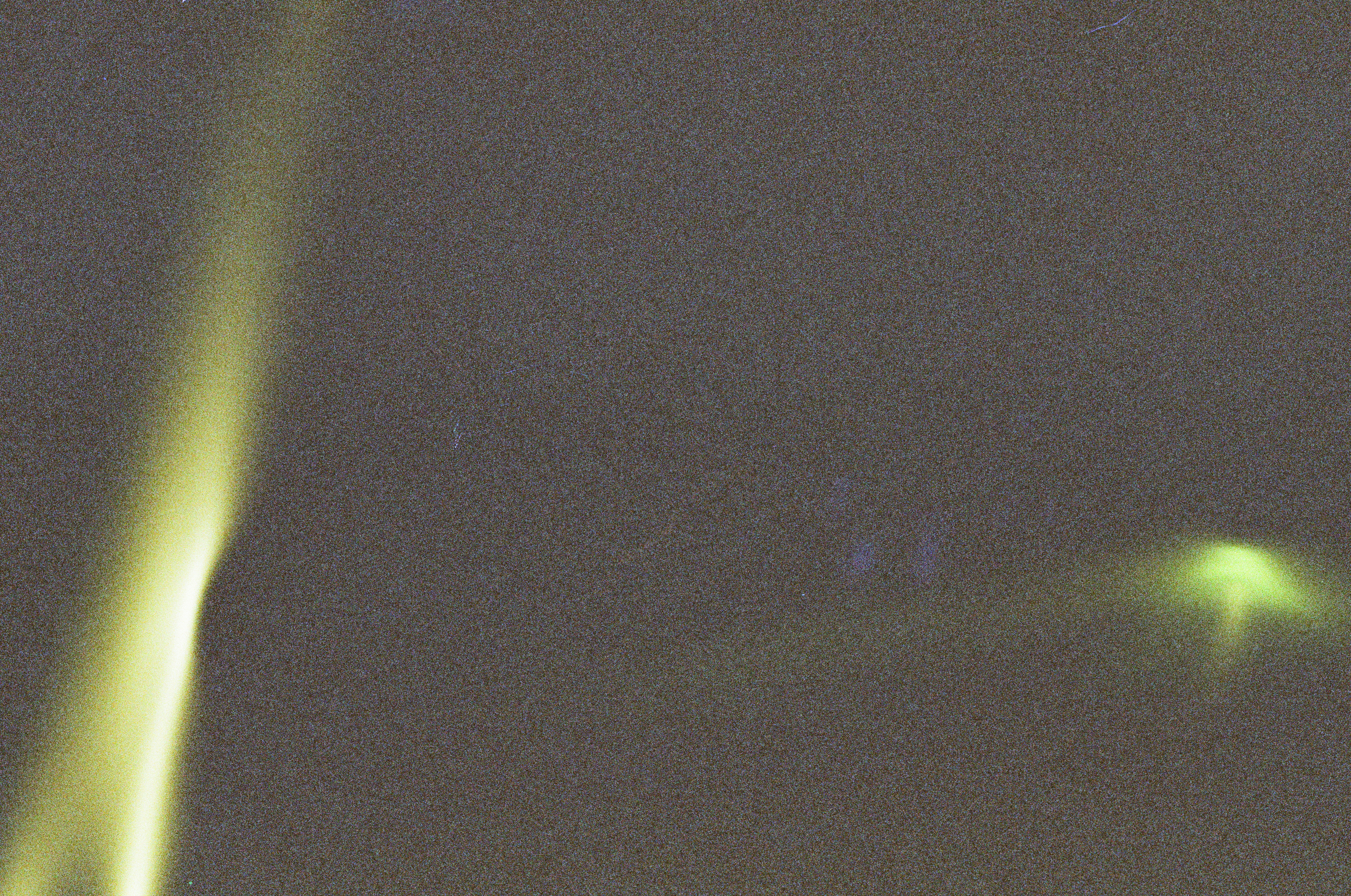 A dark, heavily grained field holds two soft yellow-green streaks of light, one angling down the left side and one entering at the right.