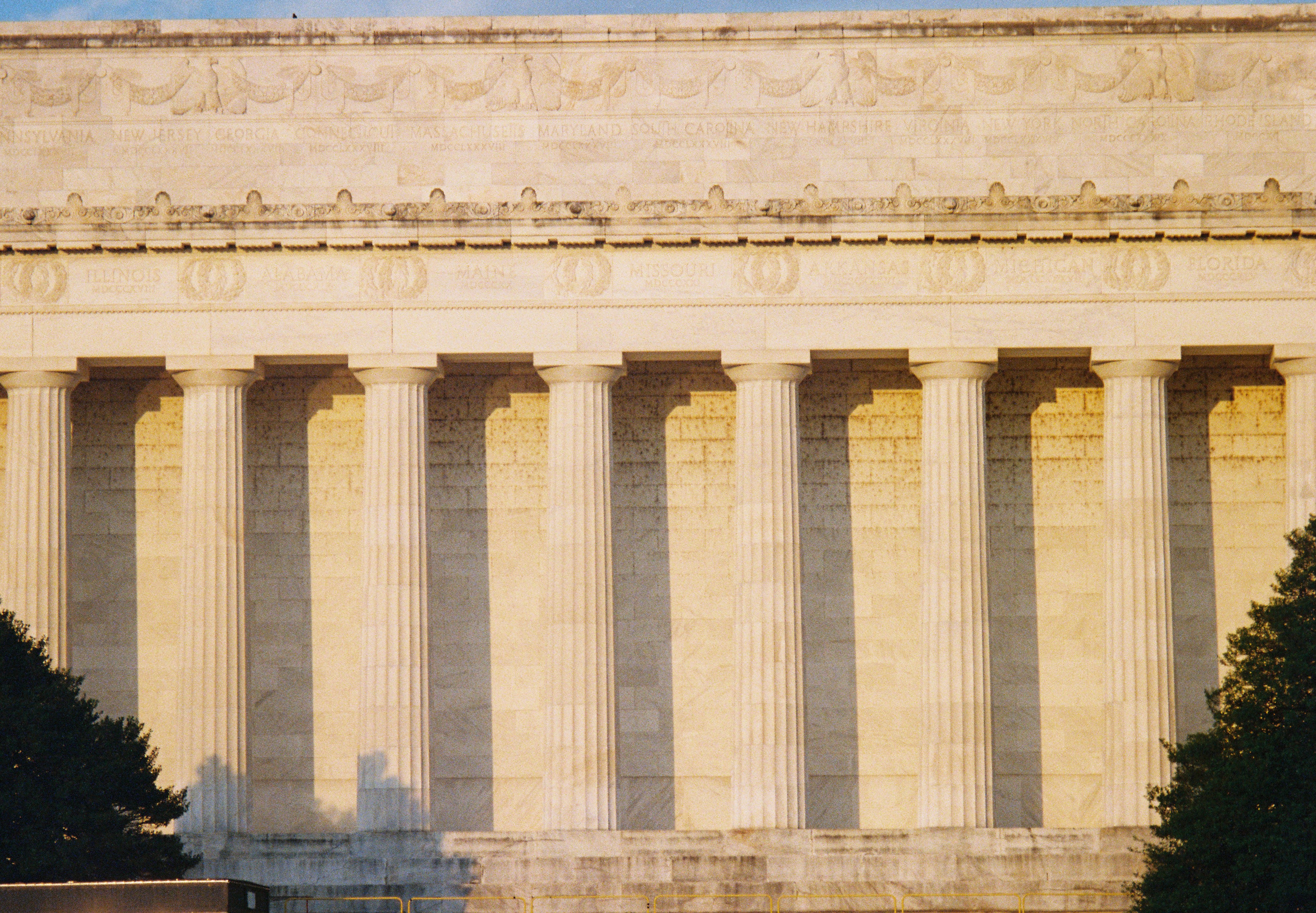 A wide run of pale columns catches golden light above dark trees and a shadowed base.
