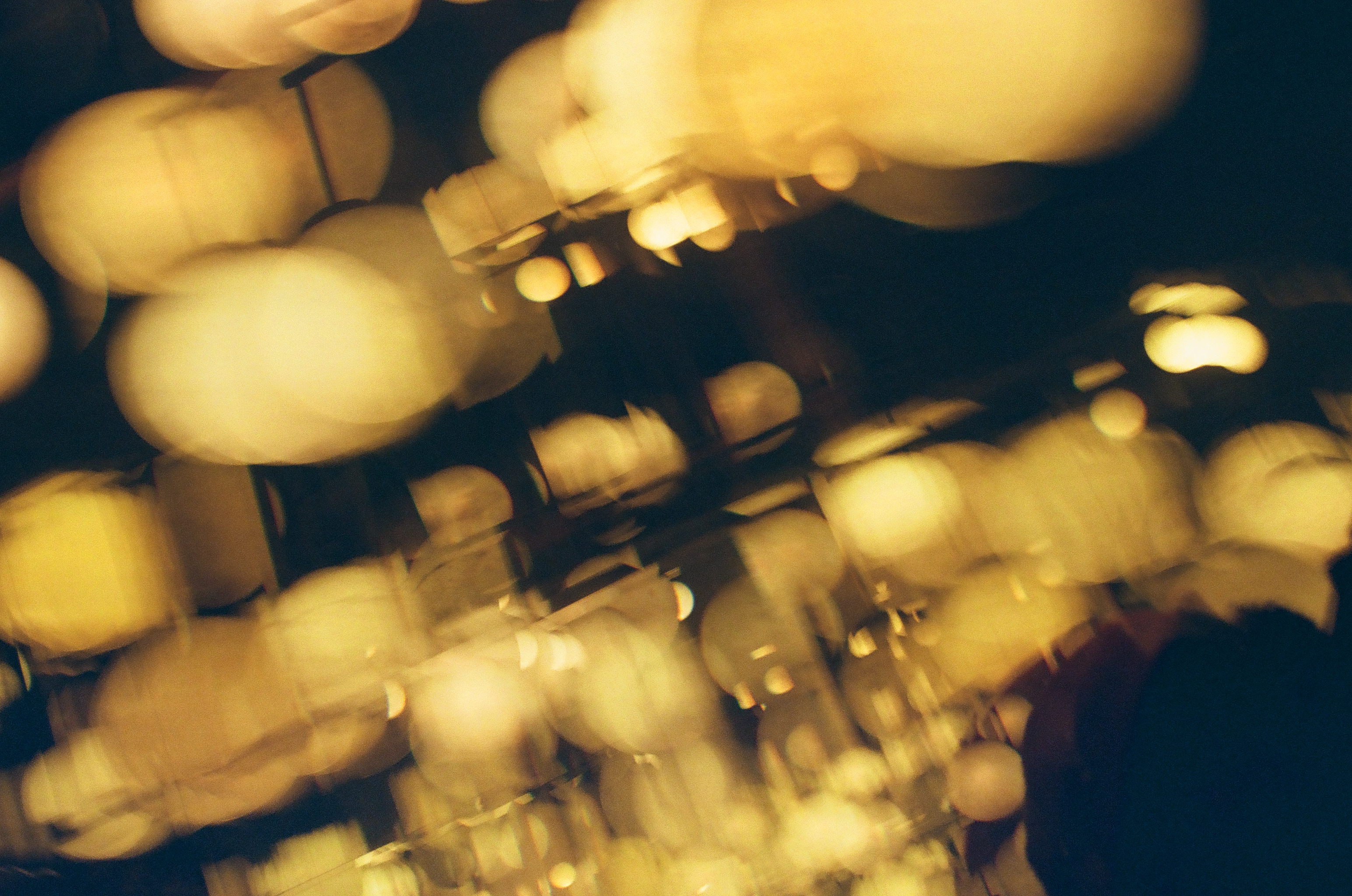 Overlapping globe lamps blur into soft golden streaks from camera motion, their round shapes smearing across the dark frame.
