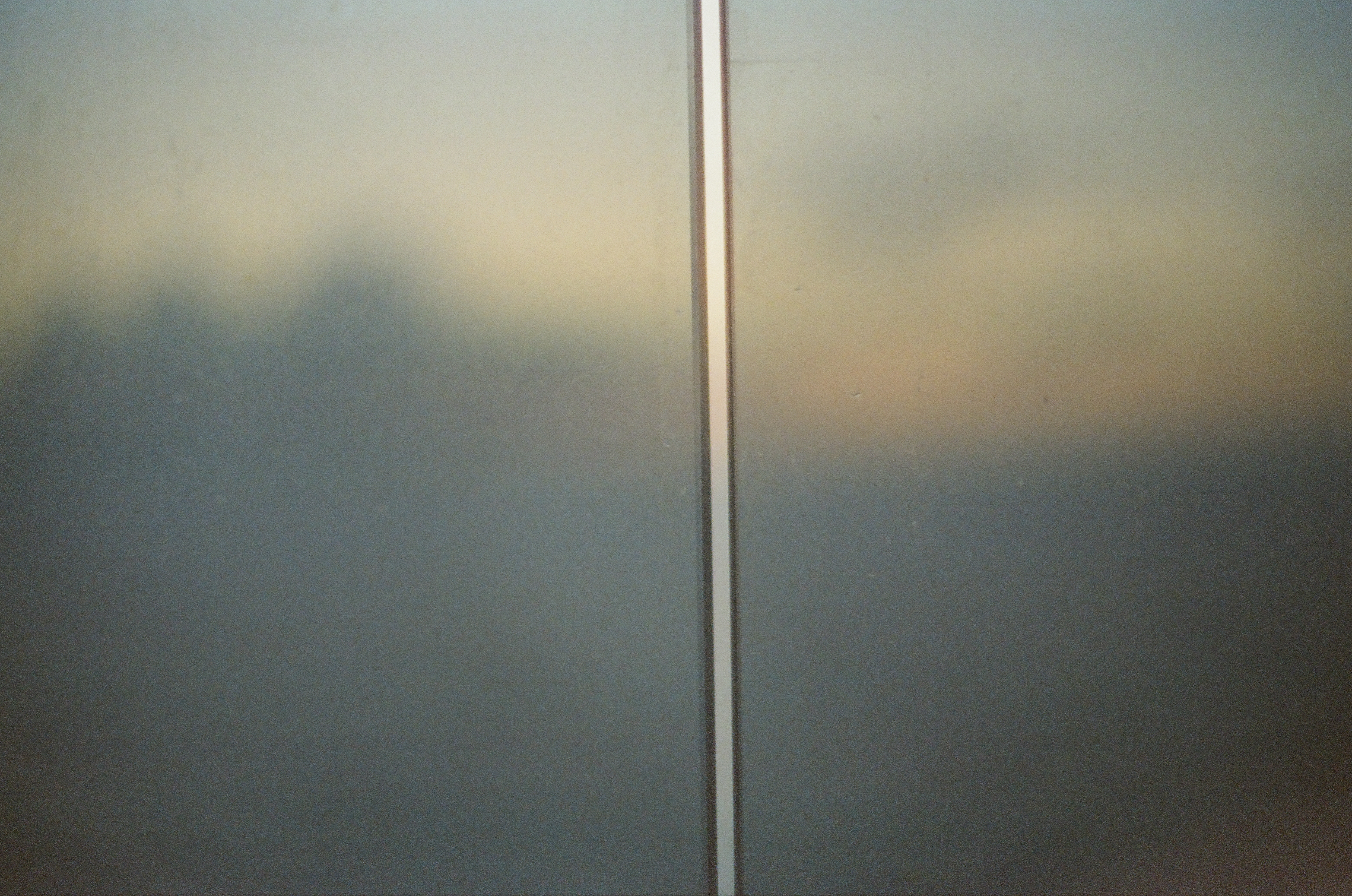 A thin bright vertical strip divides a hazy field of gray, green, and pale peach tones that darken toward the bottom of the frame.