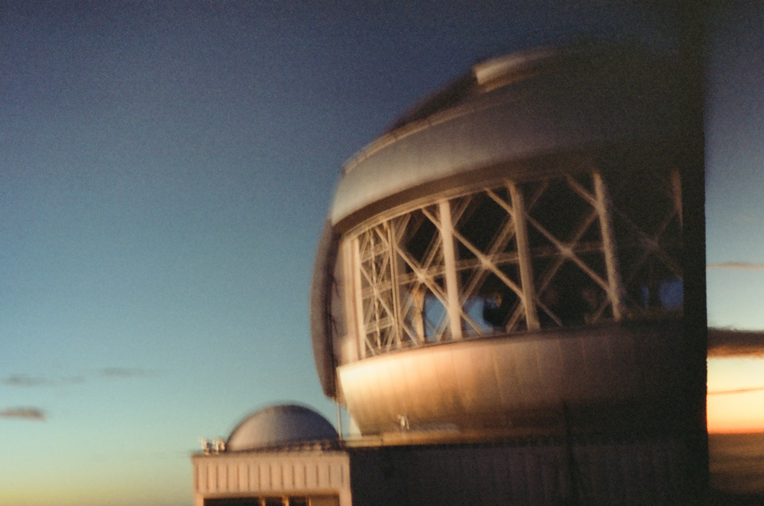 A pale observatory dome reveals a curved interior lattice against a fading blue and orange sky.