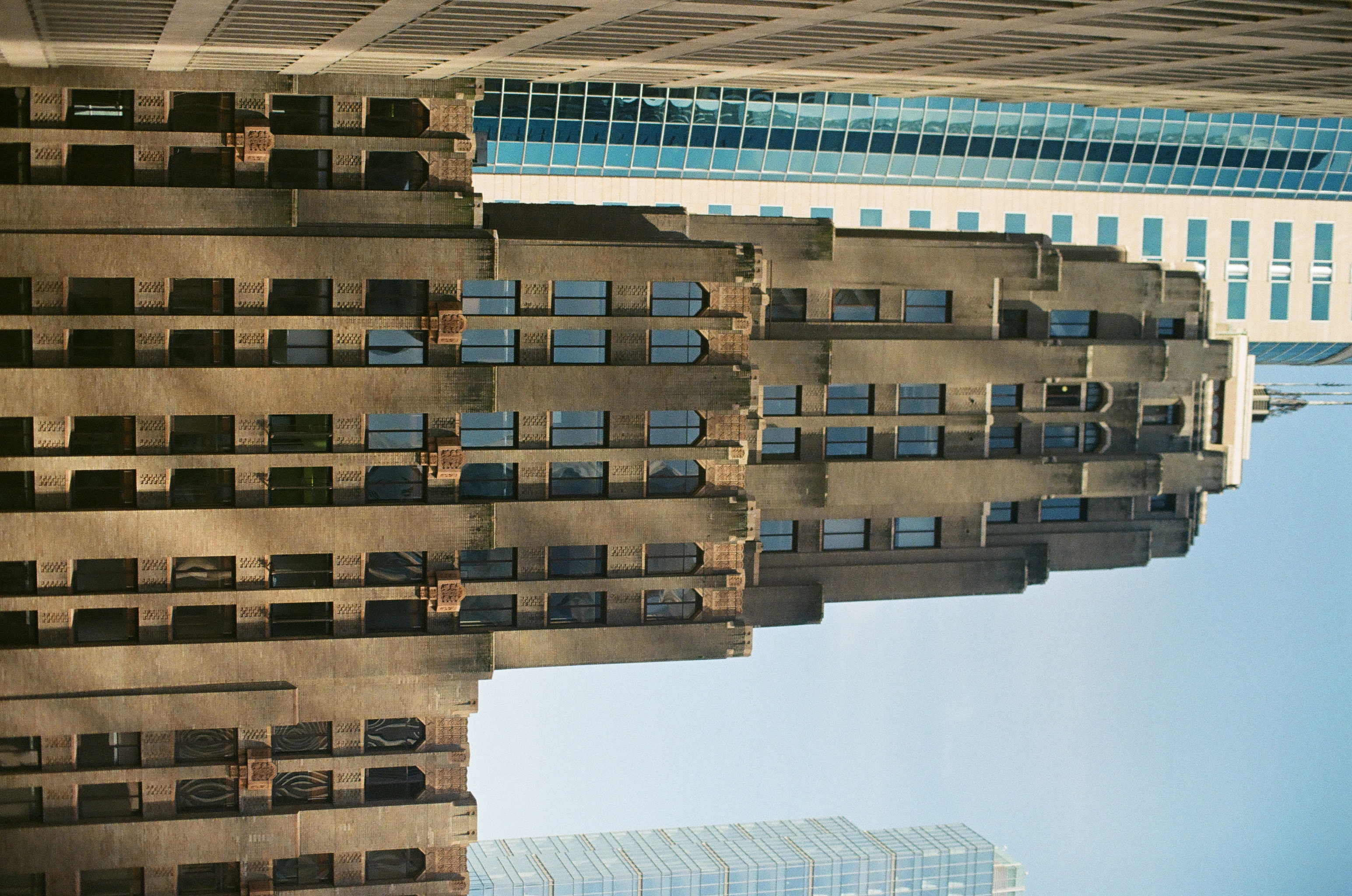 A tall brown stepped tower rises between pale modern buildings under clear daylight.