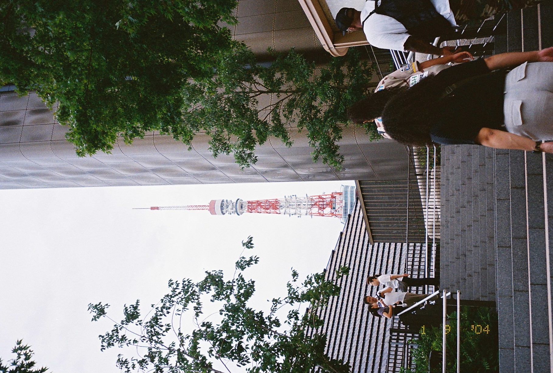A broad stone staircase leads up toward a red-and-white lattice tower visible between trees and a curved metal-clad building.