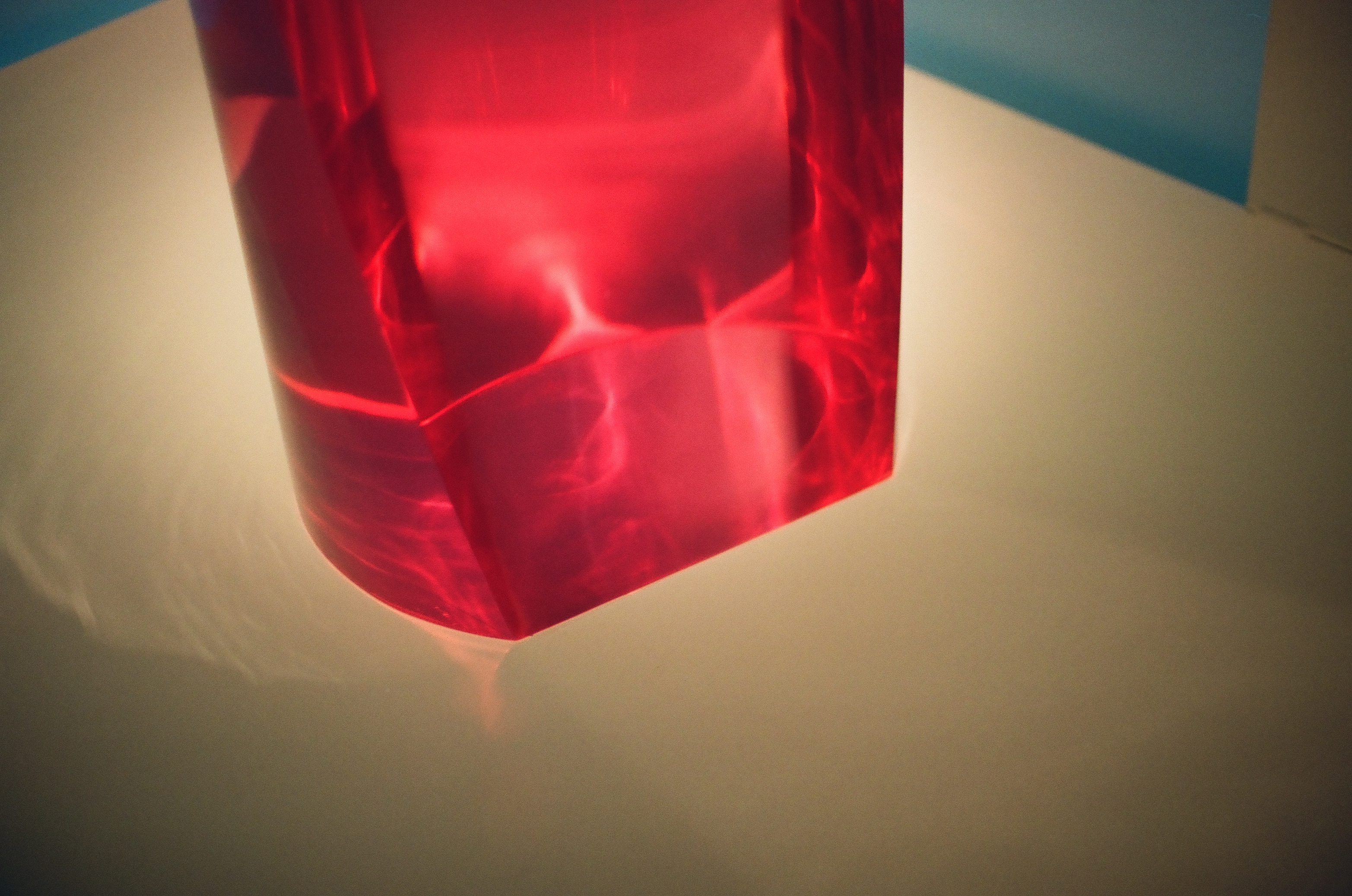 The lower portion of a translucent red block rests on a bright white surface, casting a pink glow across it.