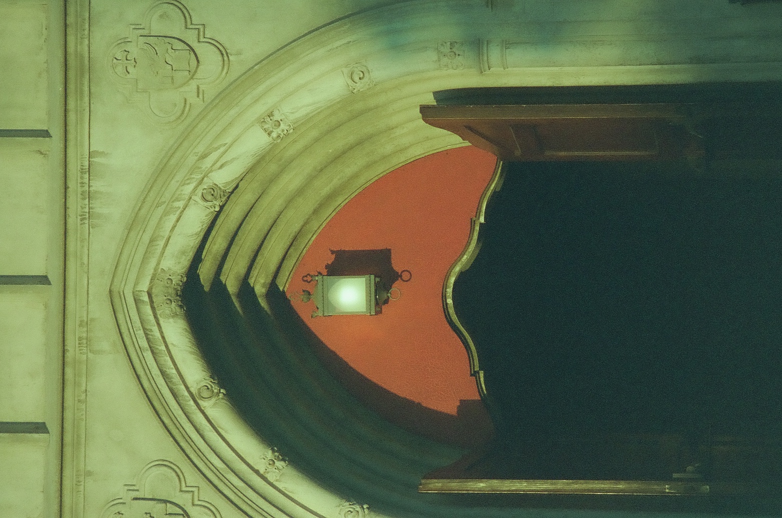 A carved pointed stone arch surrounds an open doorway and red inner wall beneath a small hanging lantern.