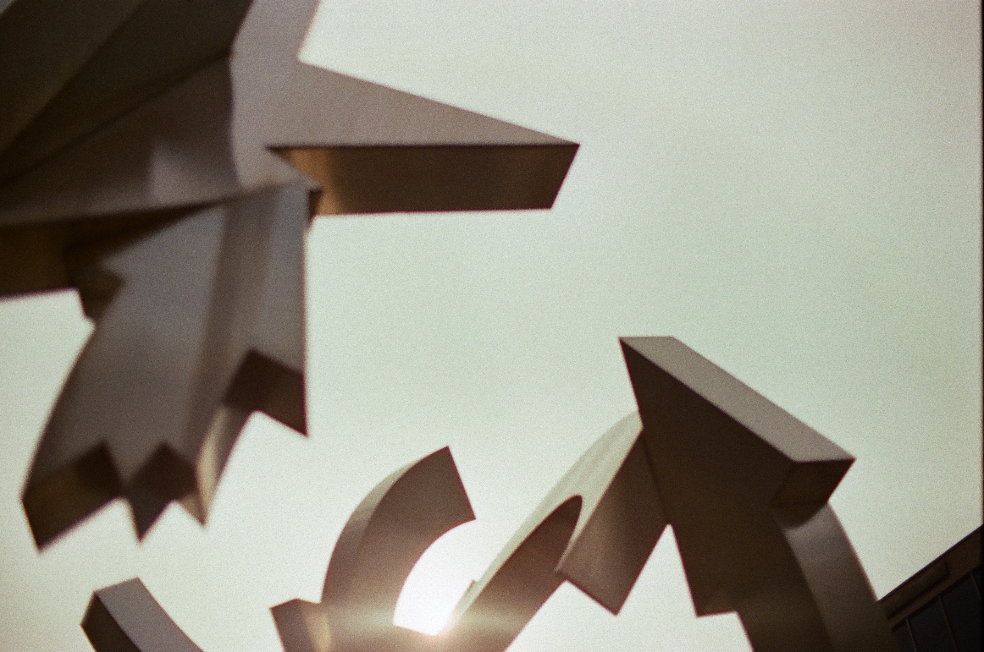 Sharp arrow-like metal forms overlap beneath a broad dark slab against pale open sky.