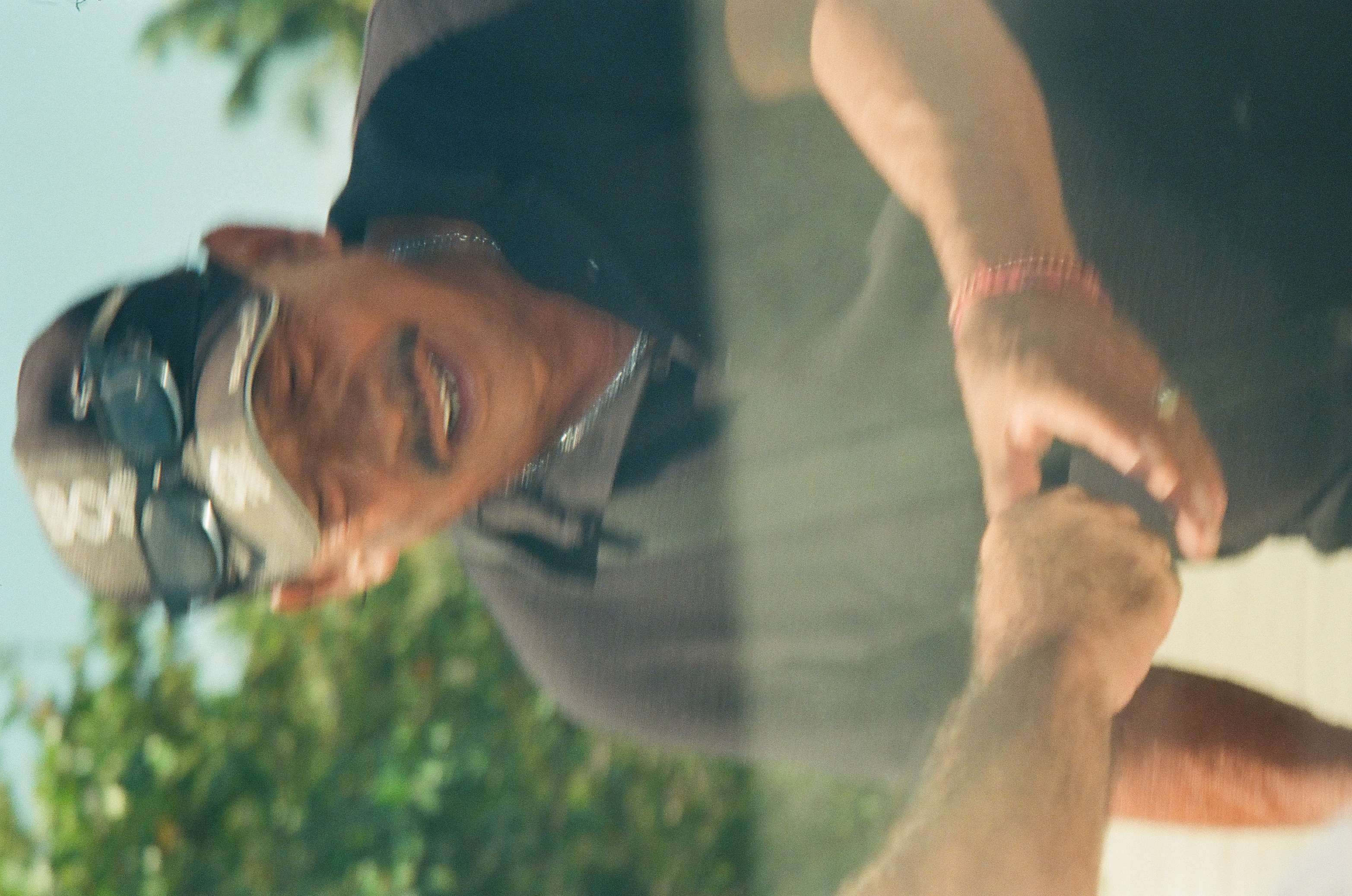 A blurred person in a dark cap and shirt leans forward as two soft-focused hands meet beneath a pale translucent band.