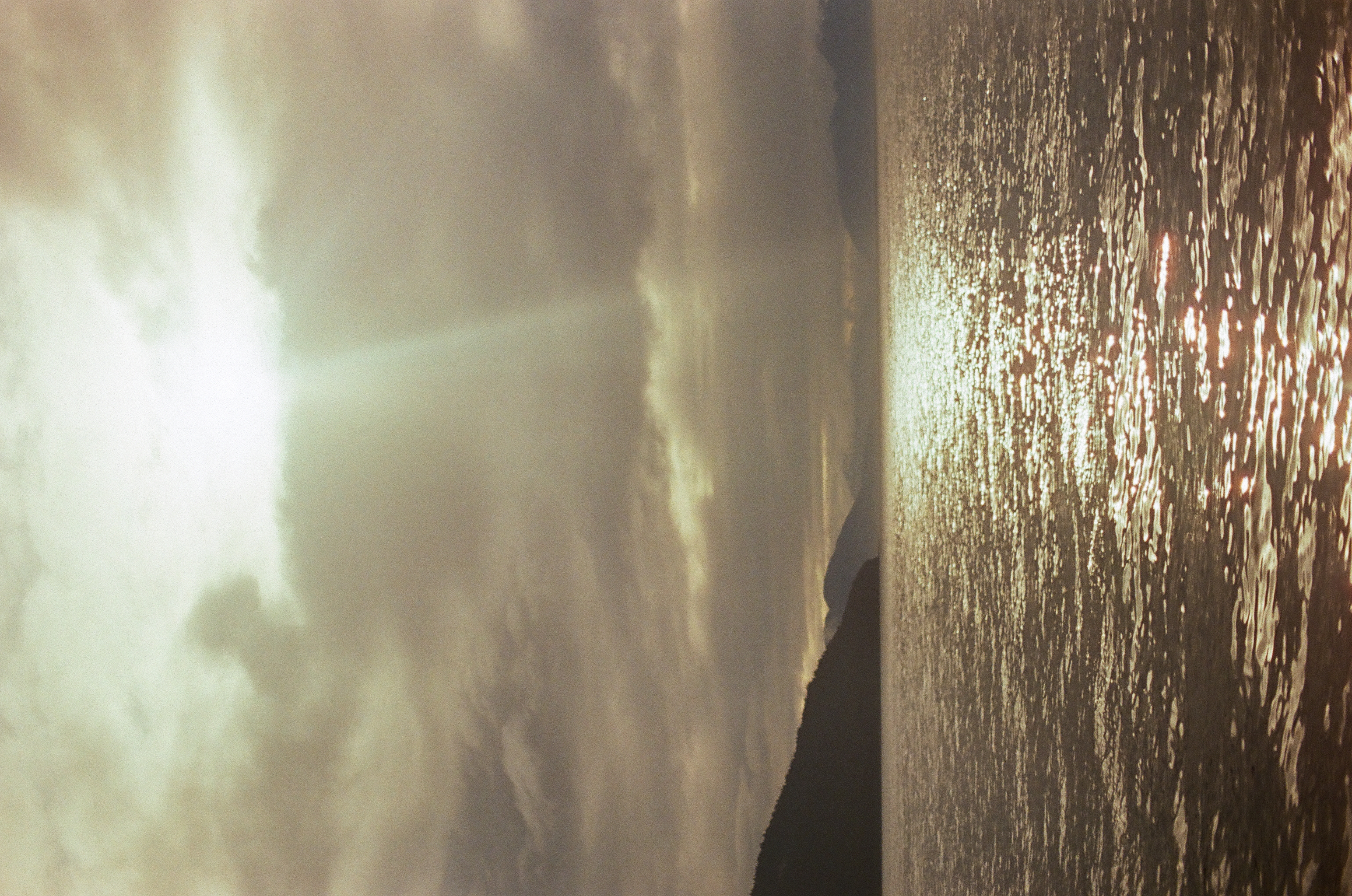 A vertical shaft of light breaks layered clouds and crosses reflective water between dark landforms.