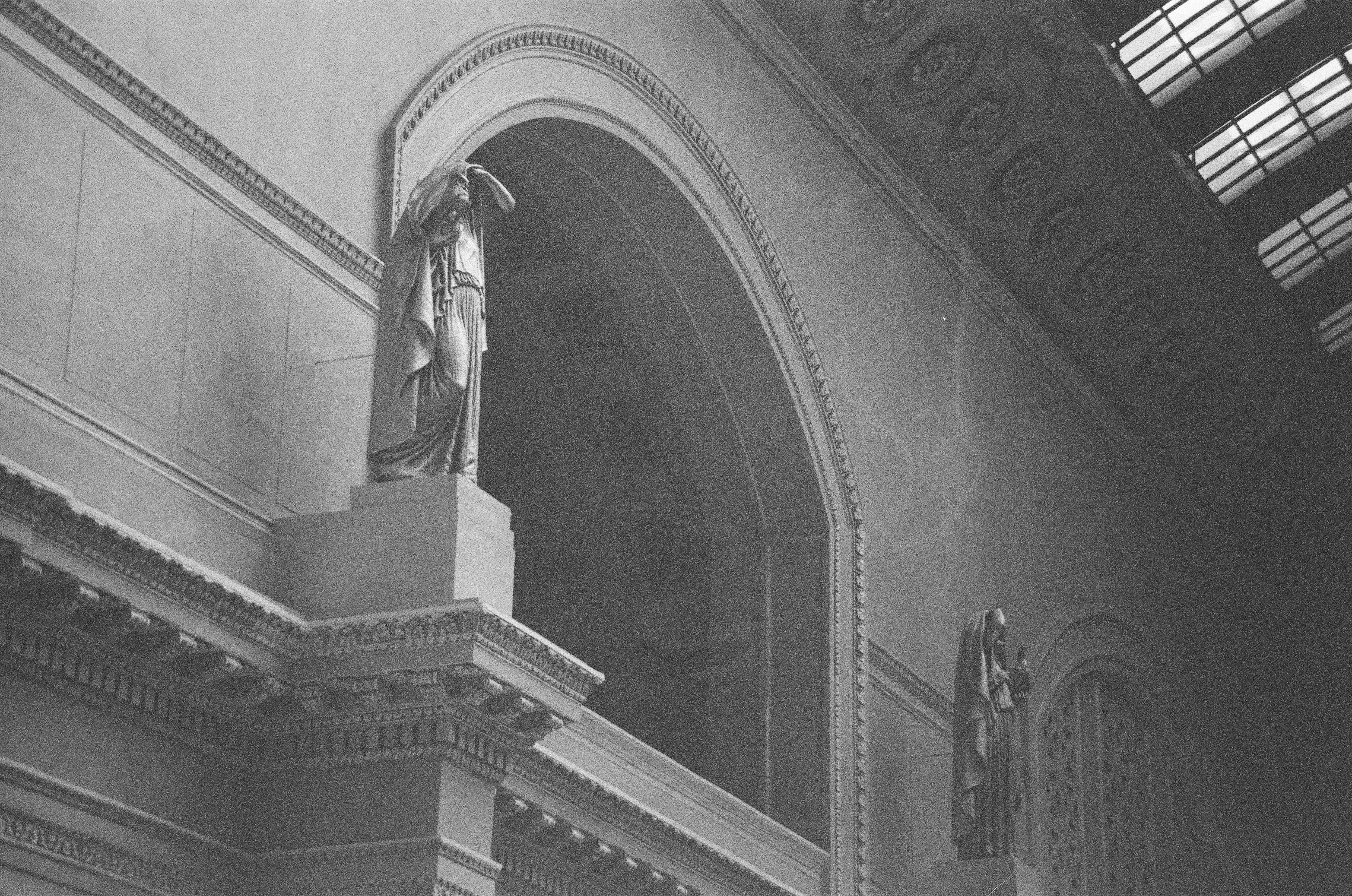 A standing statue occupies the spring of a broad arch beneath patterned stonework and a bright glazed roof.