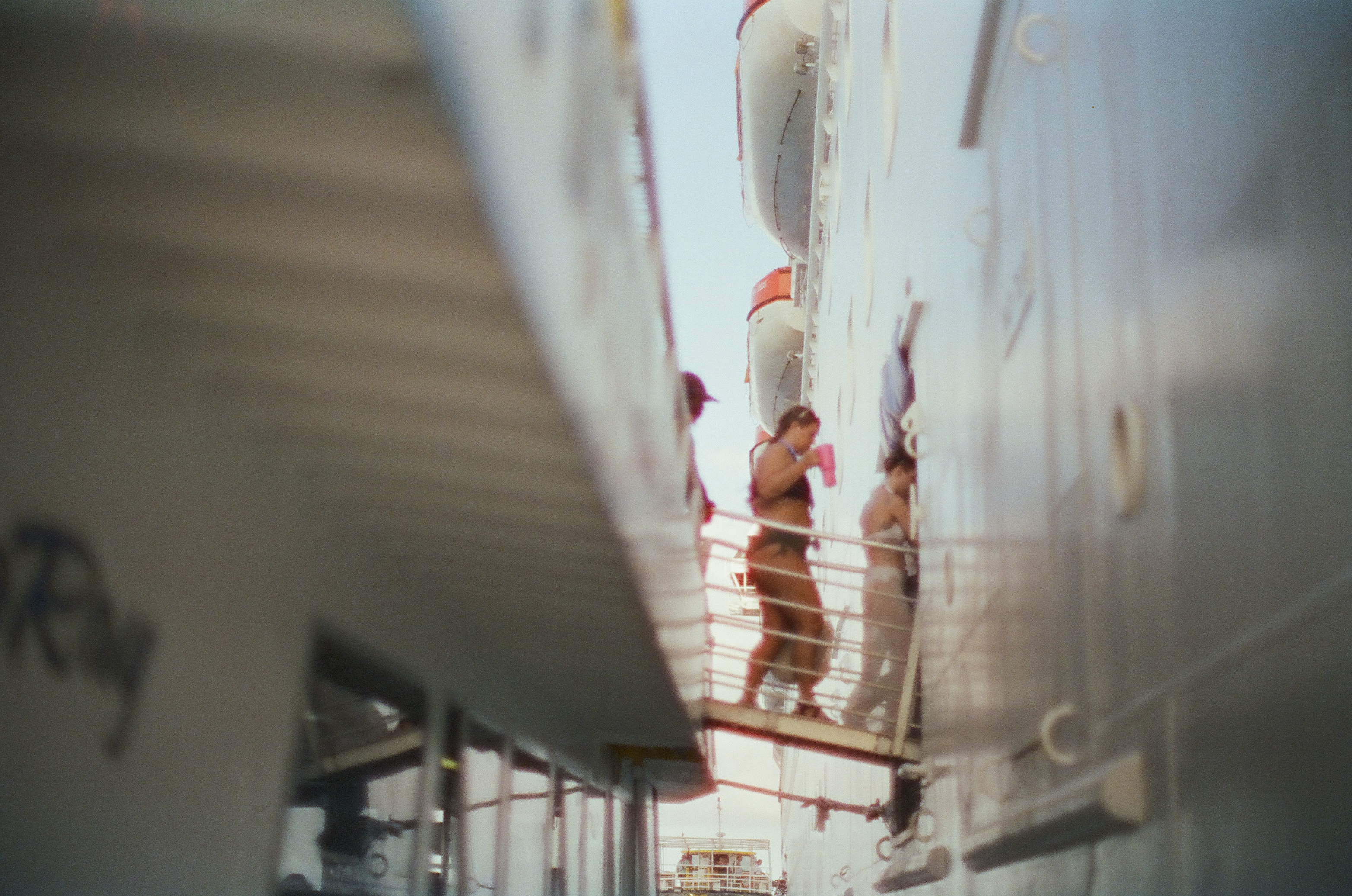 Adults stand on a railed platform between blurred white structures, with lifeboats mounted above at right.