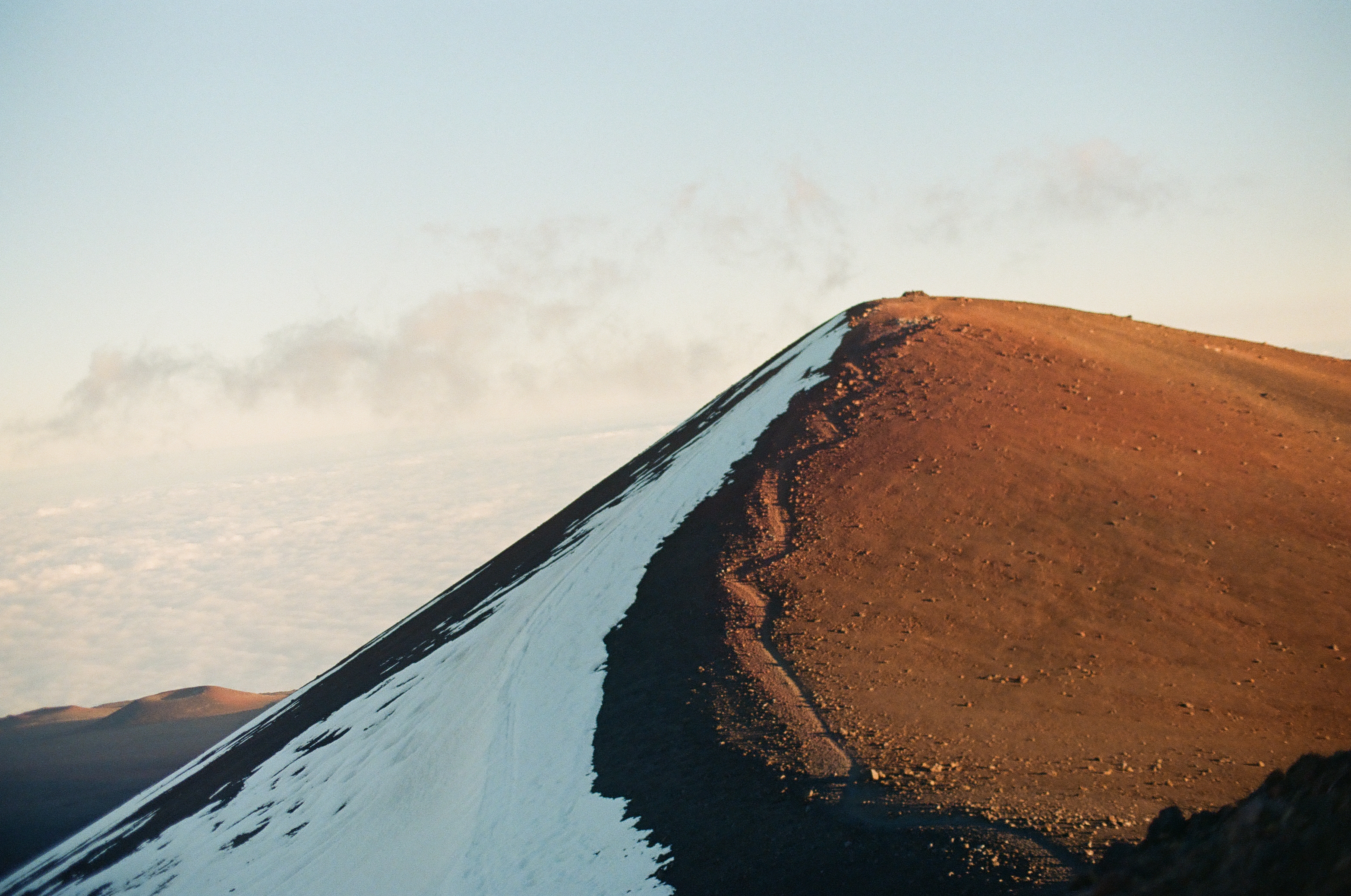 A bright wedge of snow divides a dark slope from a rust-colored sunlit summit.