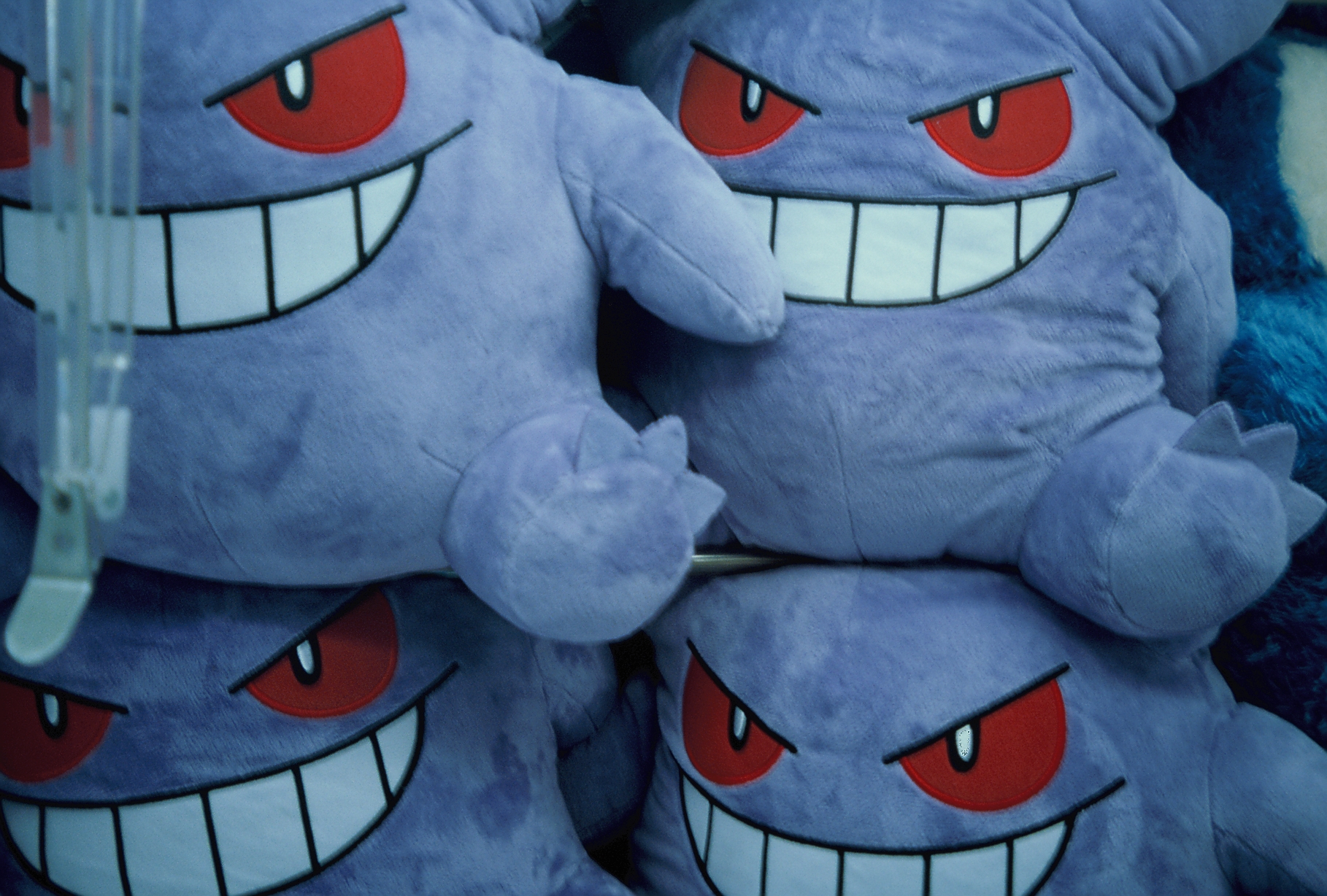 Purple plush toys with red eyes and wide toothy grins are piled together behind glass, with a metal claw visible at the edge.
