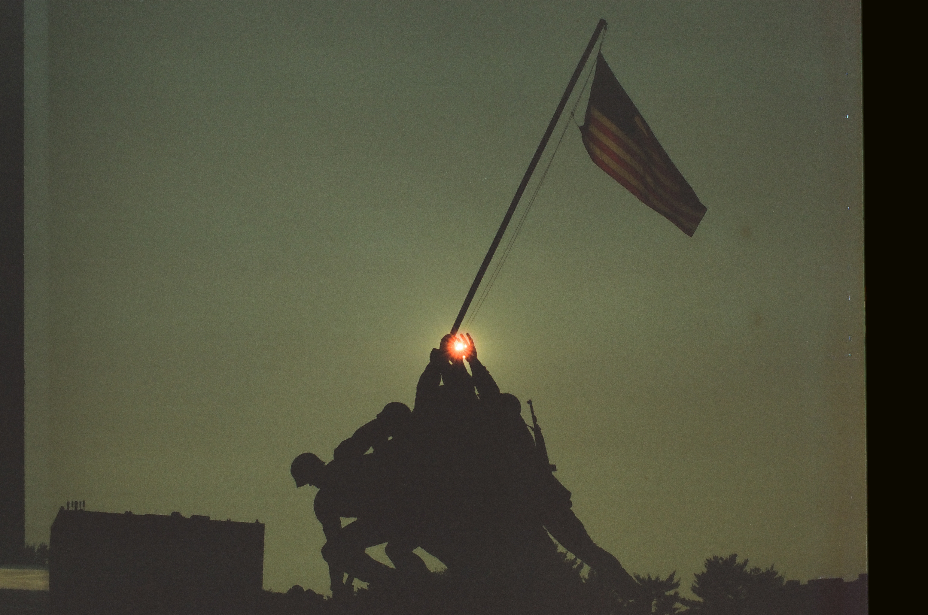 A silhouetted group raises a flag on a long pole as a red light meets its base.