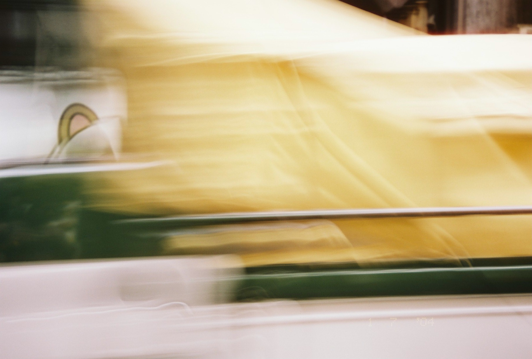 Broad horizontal bands of yellow and green motion blur dominate the frame, with a pale rounded shape visible near the left edge.