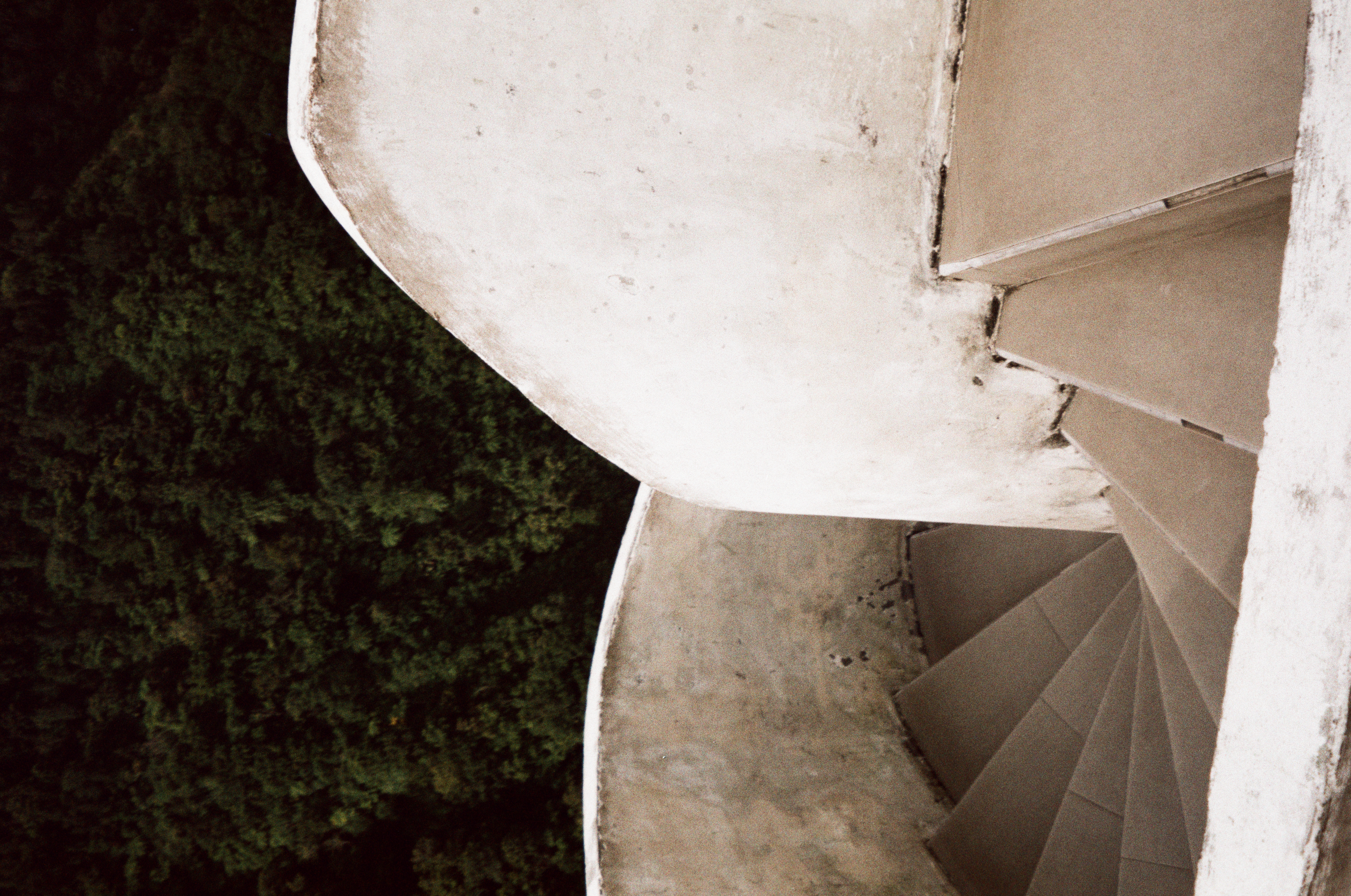 Two weathered white stair enclosures overlap against dark green trees, revealing wedge-shaped tiled steps in separate descending sections.