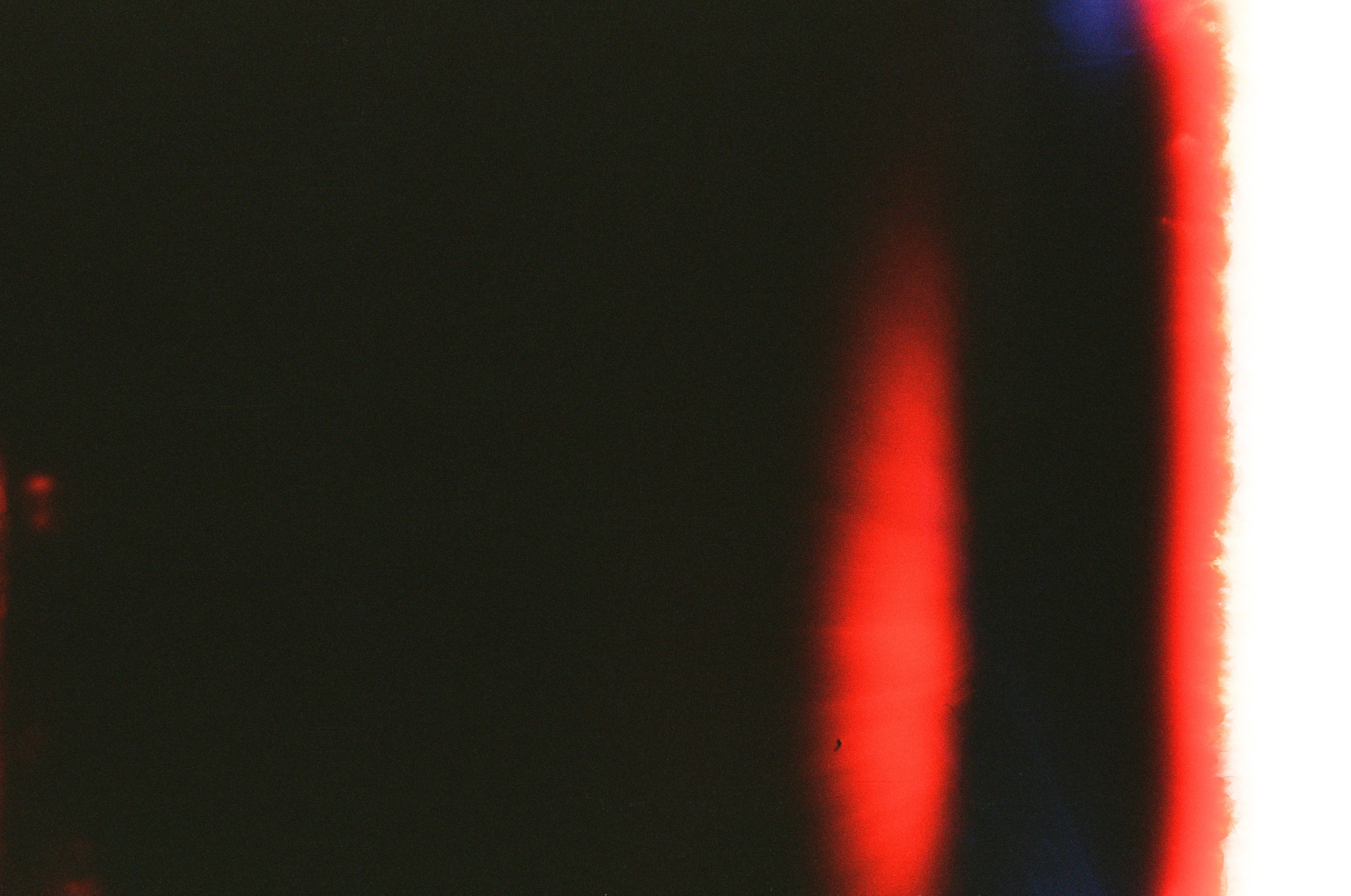 A mostly black frame contains a soft vertical red flare beside a bright white band along the right edge.