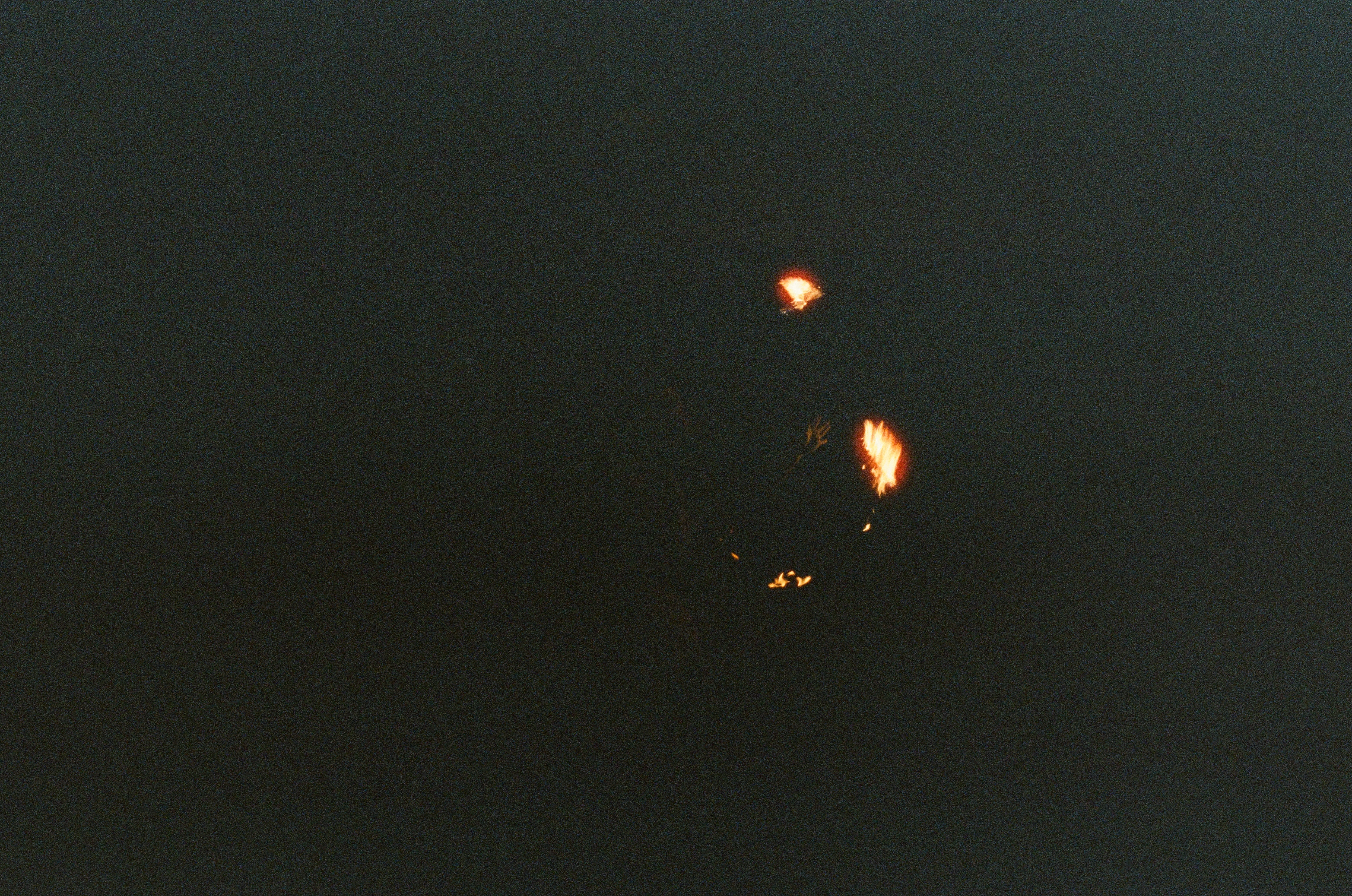Three small orange flames punctuate a nearly black night field with no ground visible.