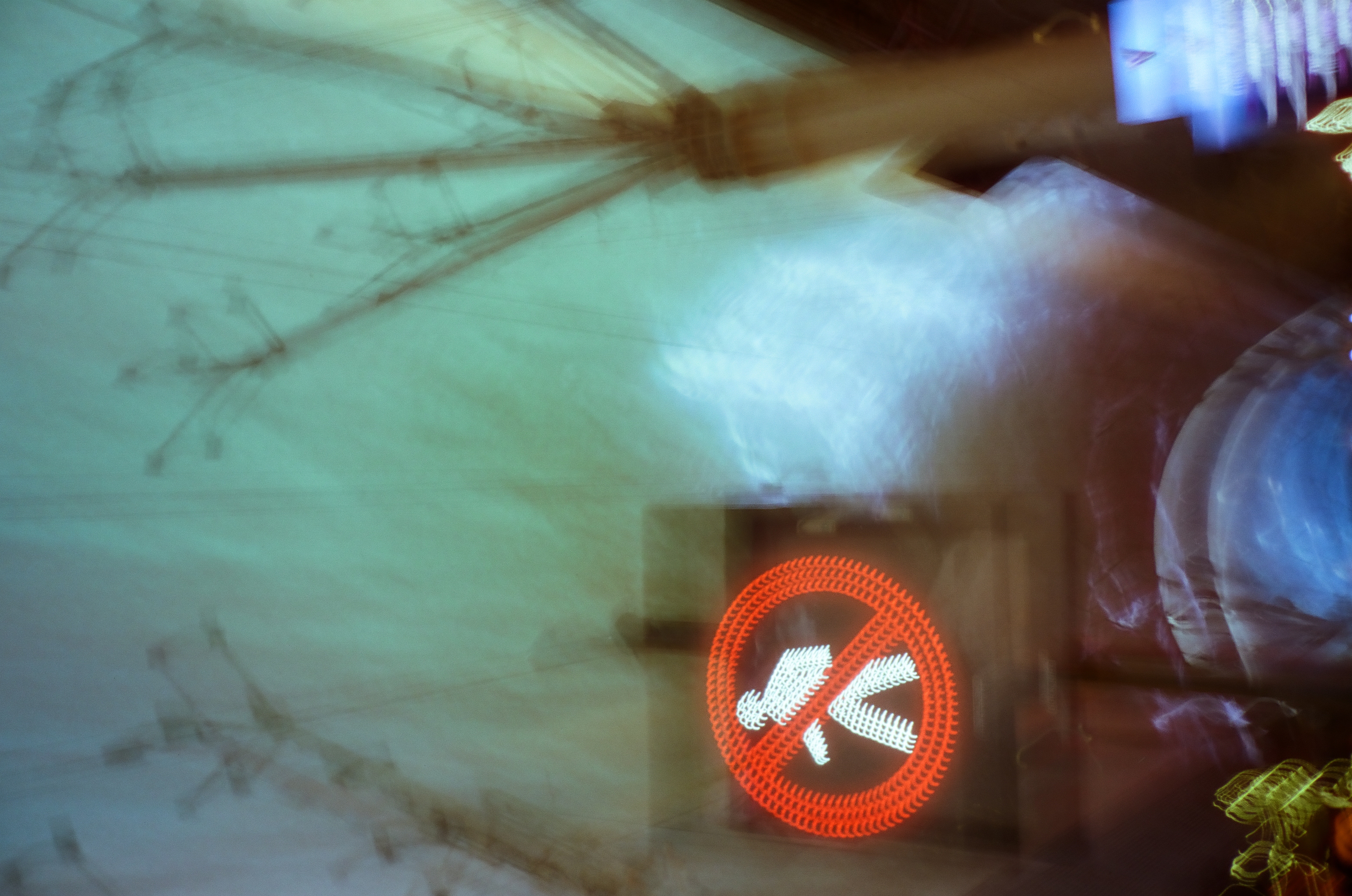 A red no-pedestrian symbol glows through a blurred double exposure of bare tree branches, a power pole, and a pale rounded shape.