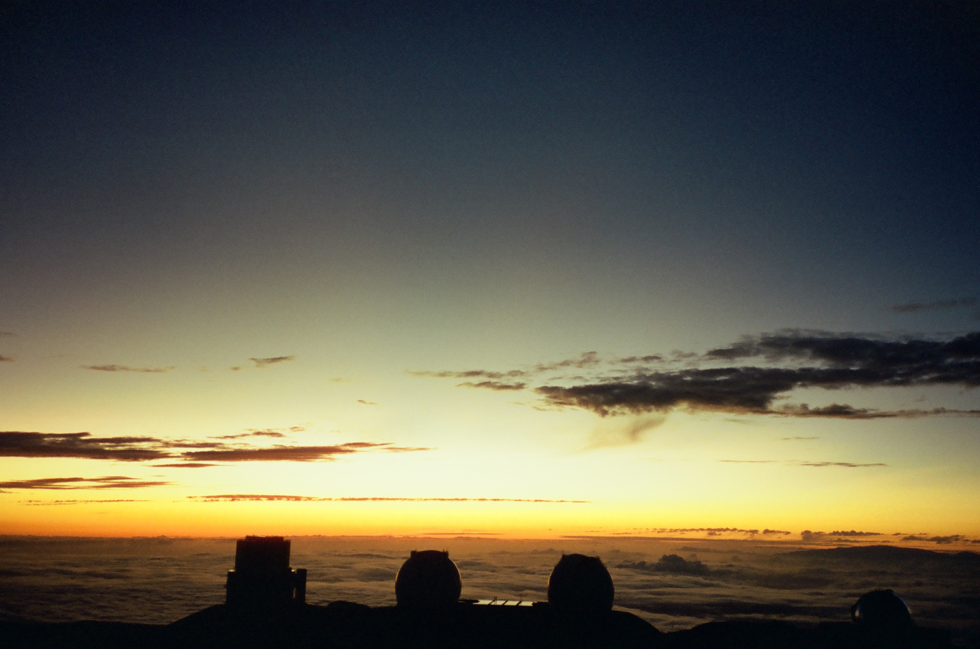 A narrow orange sunset band glows between a dark summit foreground and layered clouds.