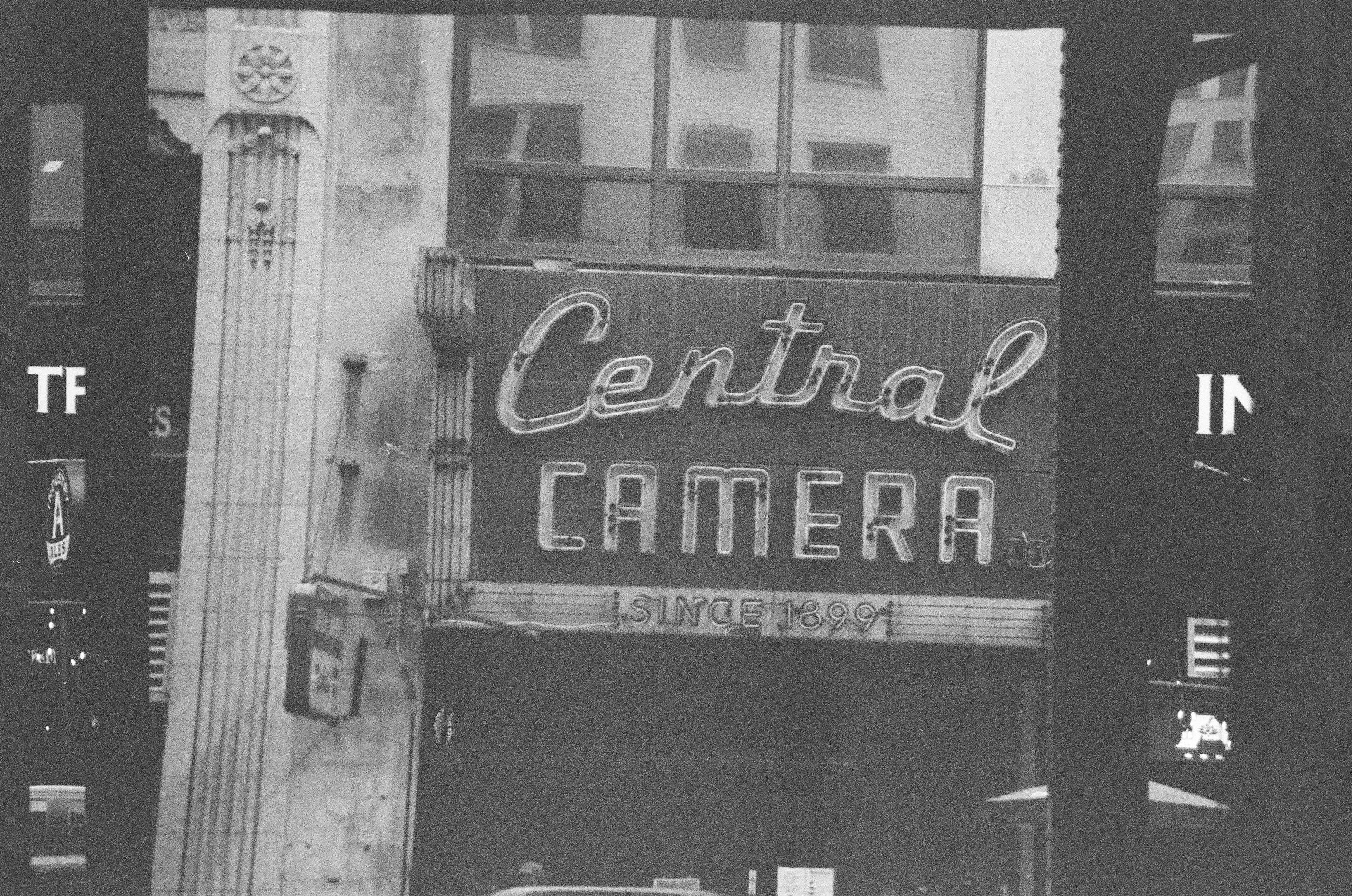 A large painted camera-shop sign appears between deep black vertical bands above a narrow storefront entrance.