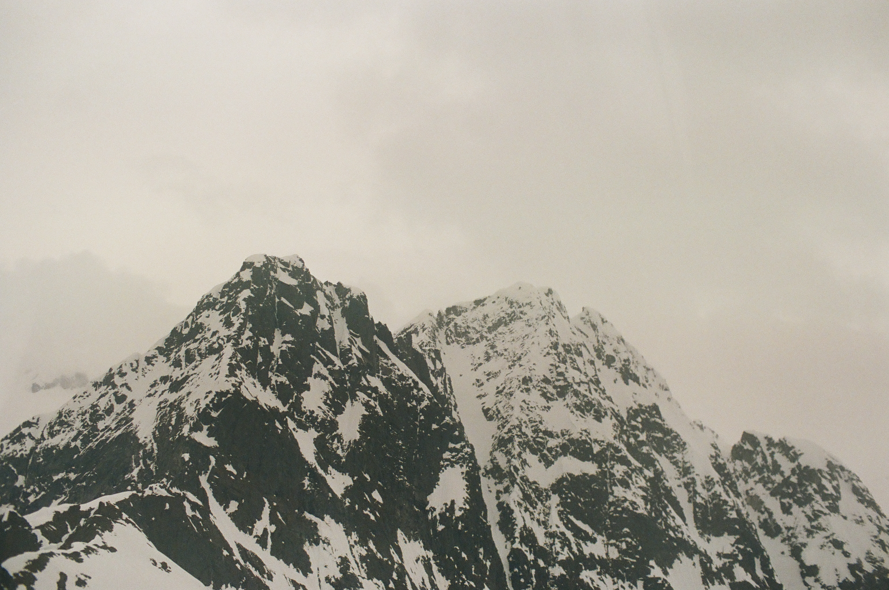 Two jagged black mountain peaks rise through white snow beneath a soft overcast sky.