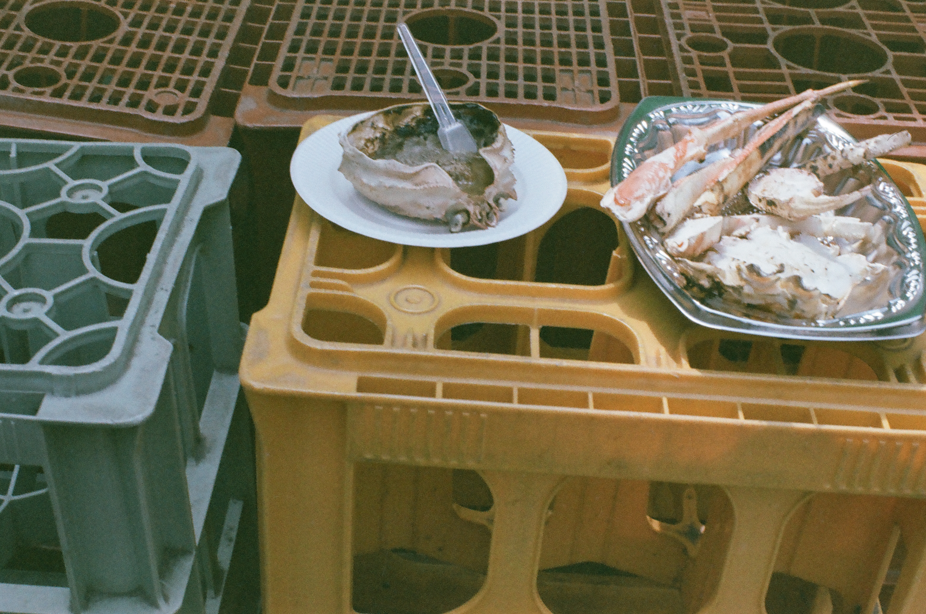 A hollowed crab shell holding an upright fork and a foil tray of picked-over crab legs sit on stacked plastic beverage crates.