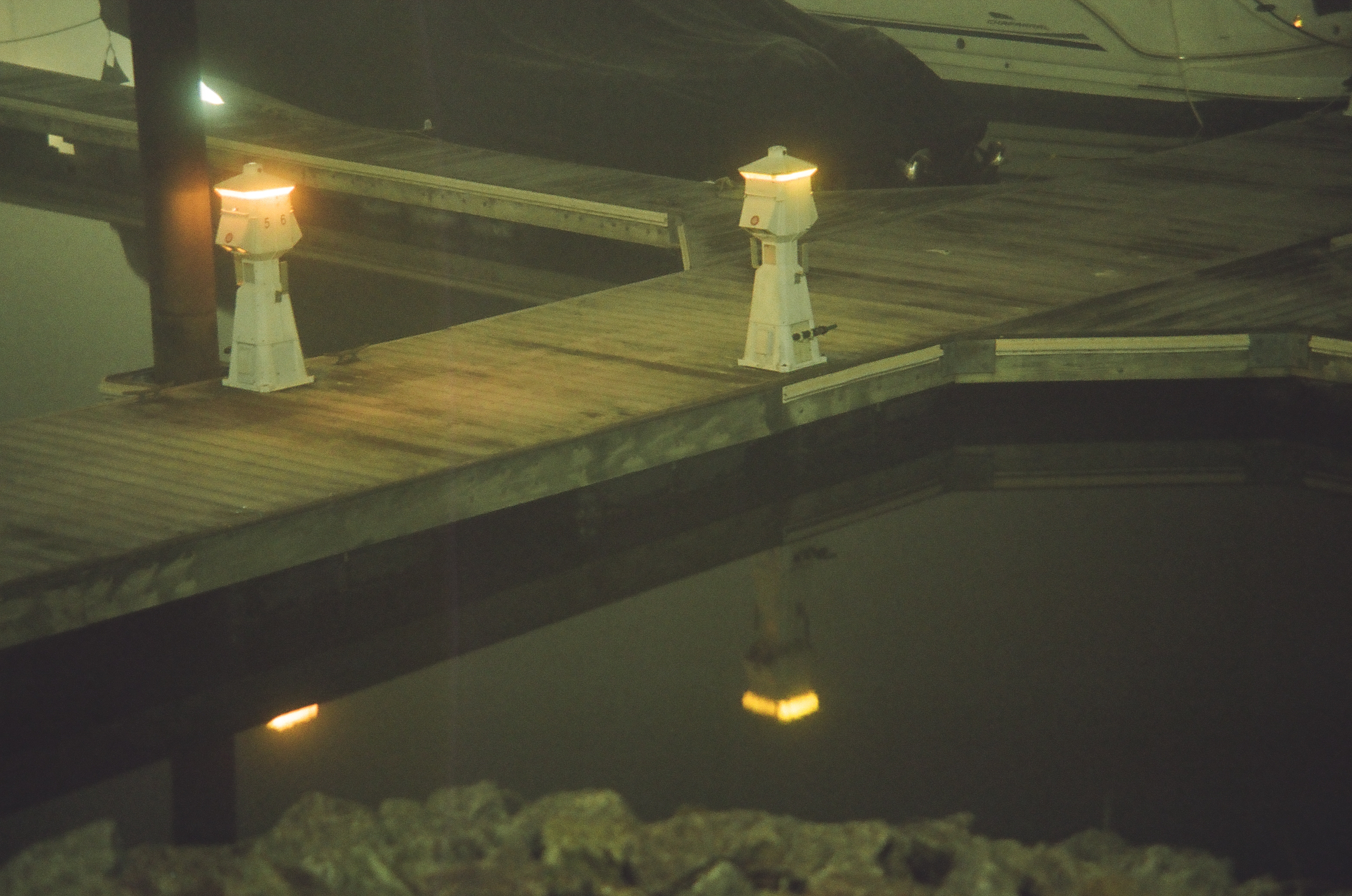 Two lighthouse-shaped dock lamps glow along a wooden pier at night, each one mirrored in the still water below.