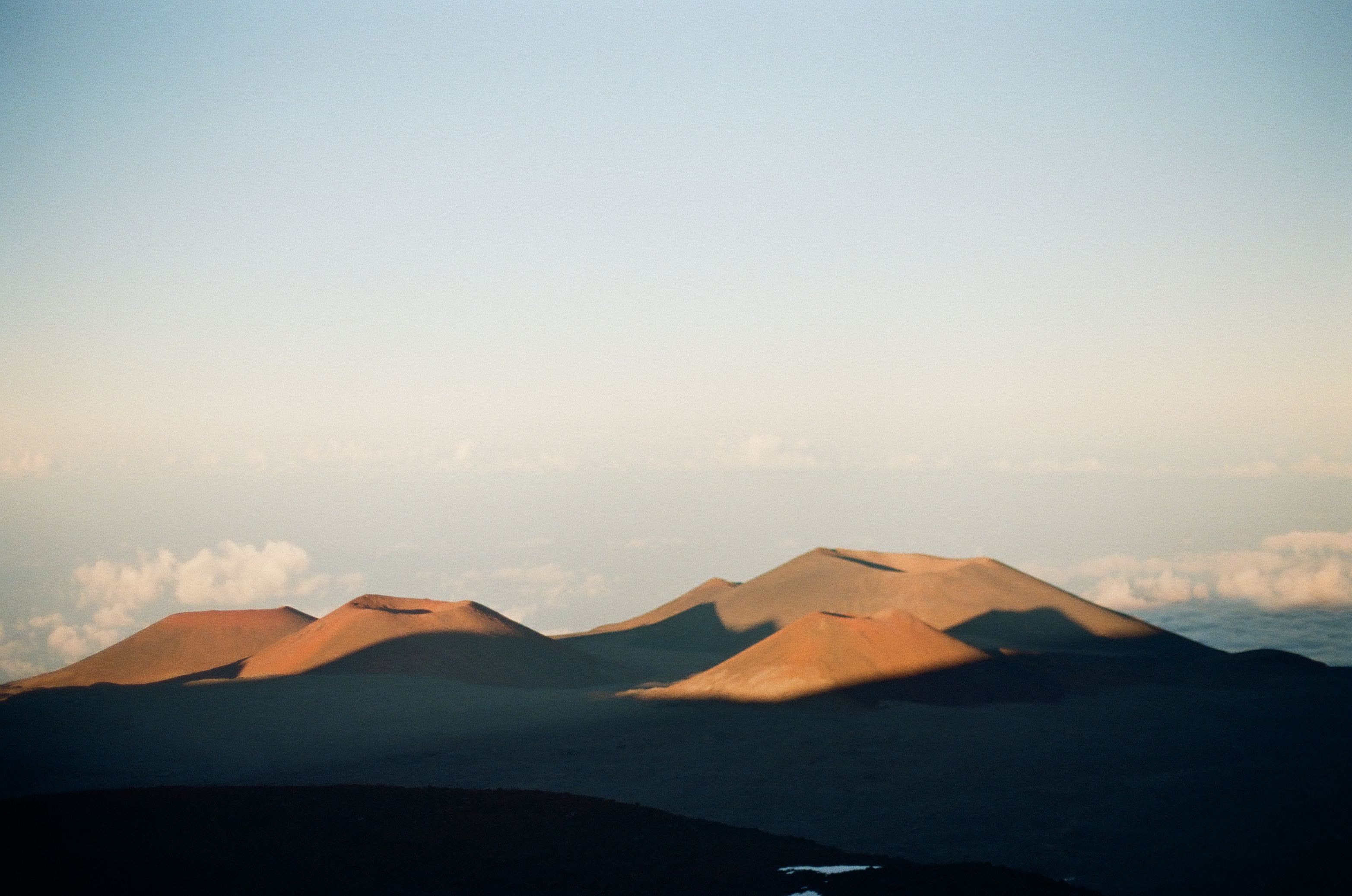 Several rounded ridges glow gold above a broad blue-black foreground and a pale cloud deck.