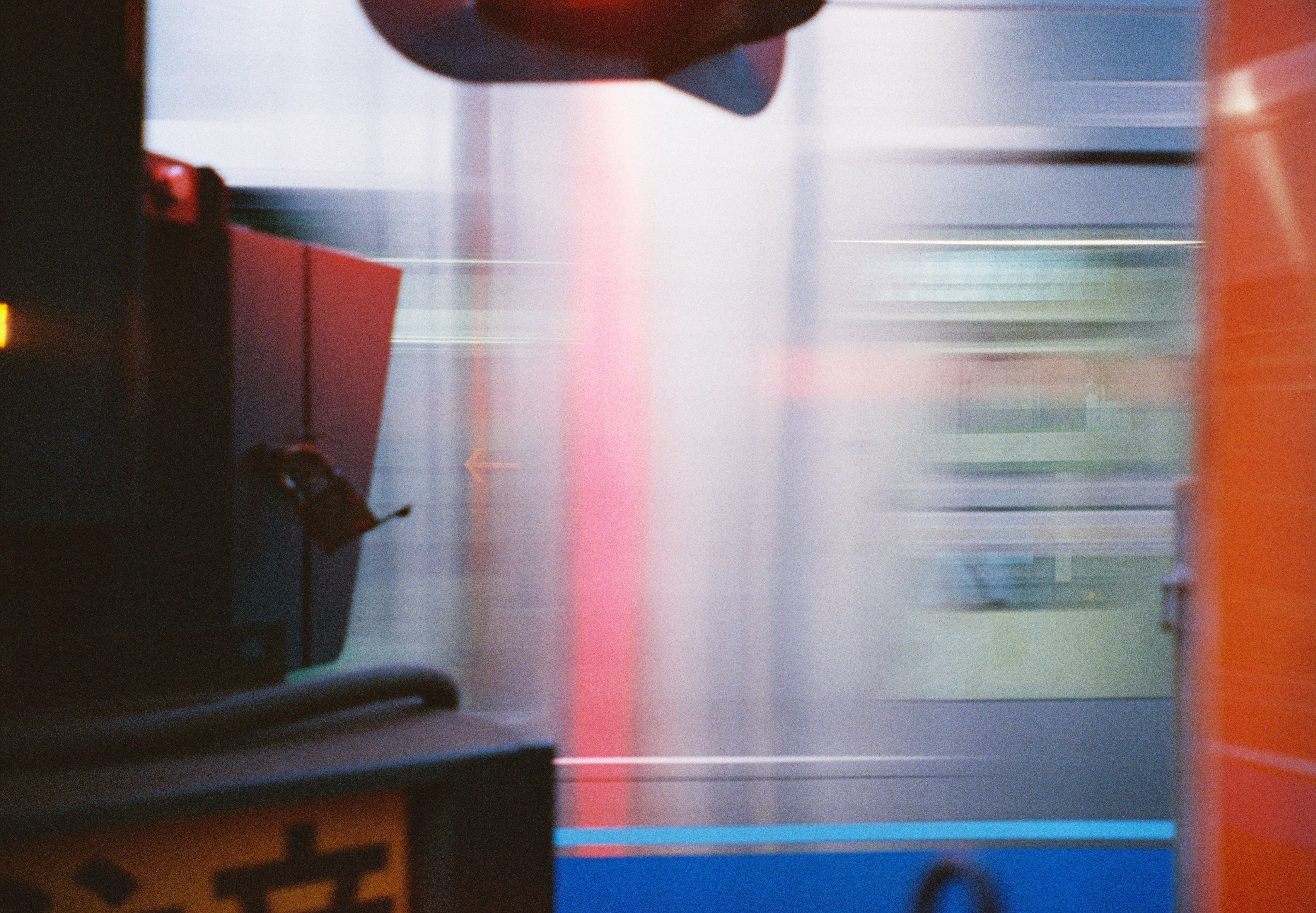 Dark signal housings on the left frame horizontal streaks of white, pink, and blue from a passing train, with an orange surface on the right.